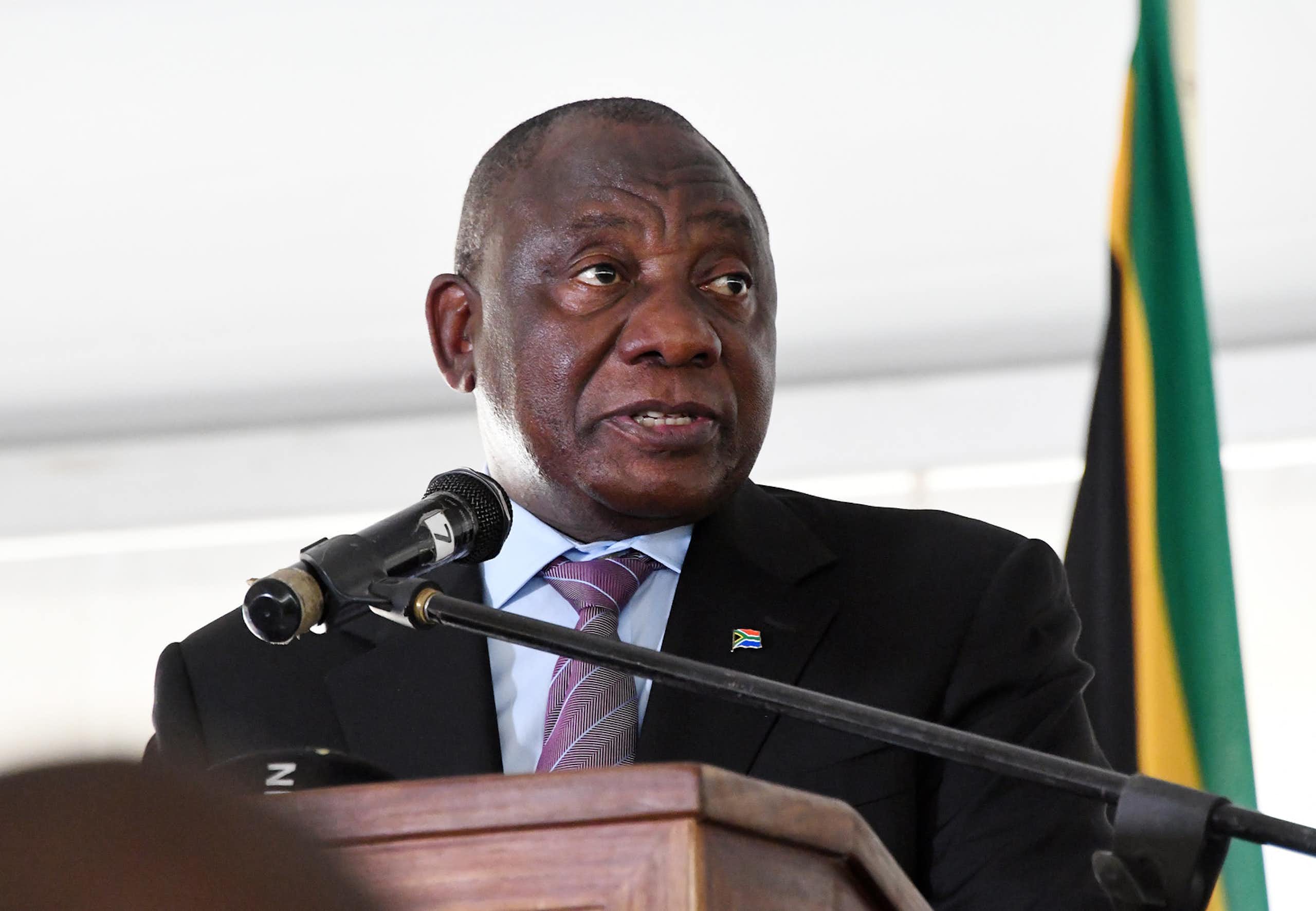 A man wearing a jacket and tie speaks into a microphone at a podium.