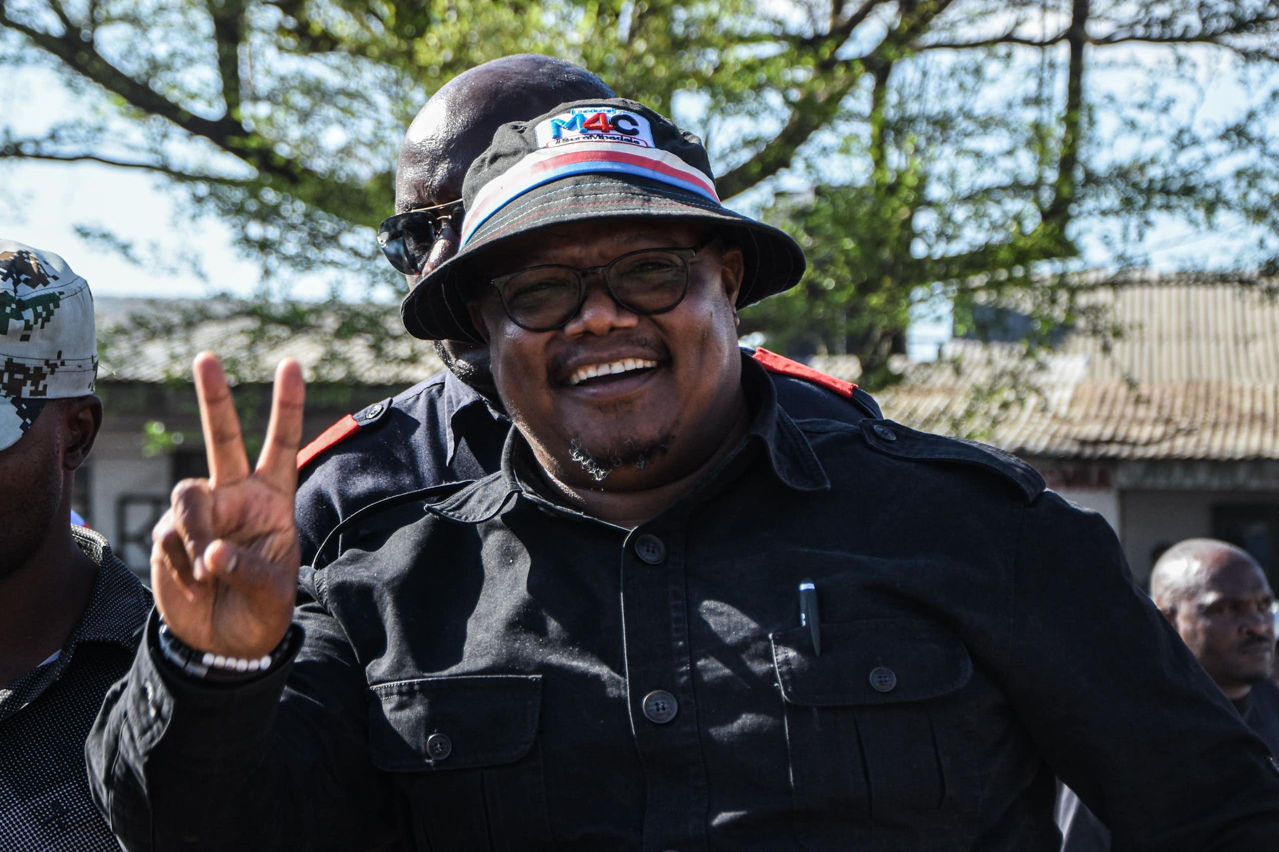 A man wearing a black cap and shirt holds up two fingers in a salute