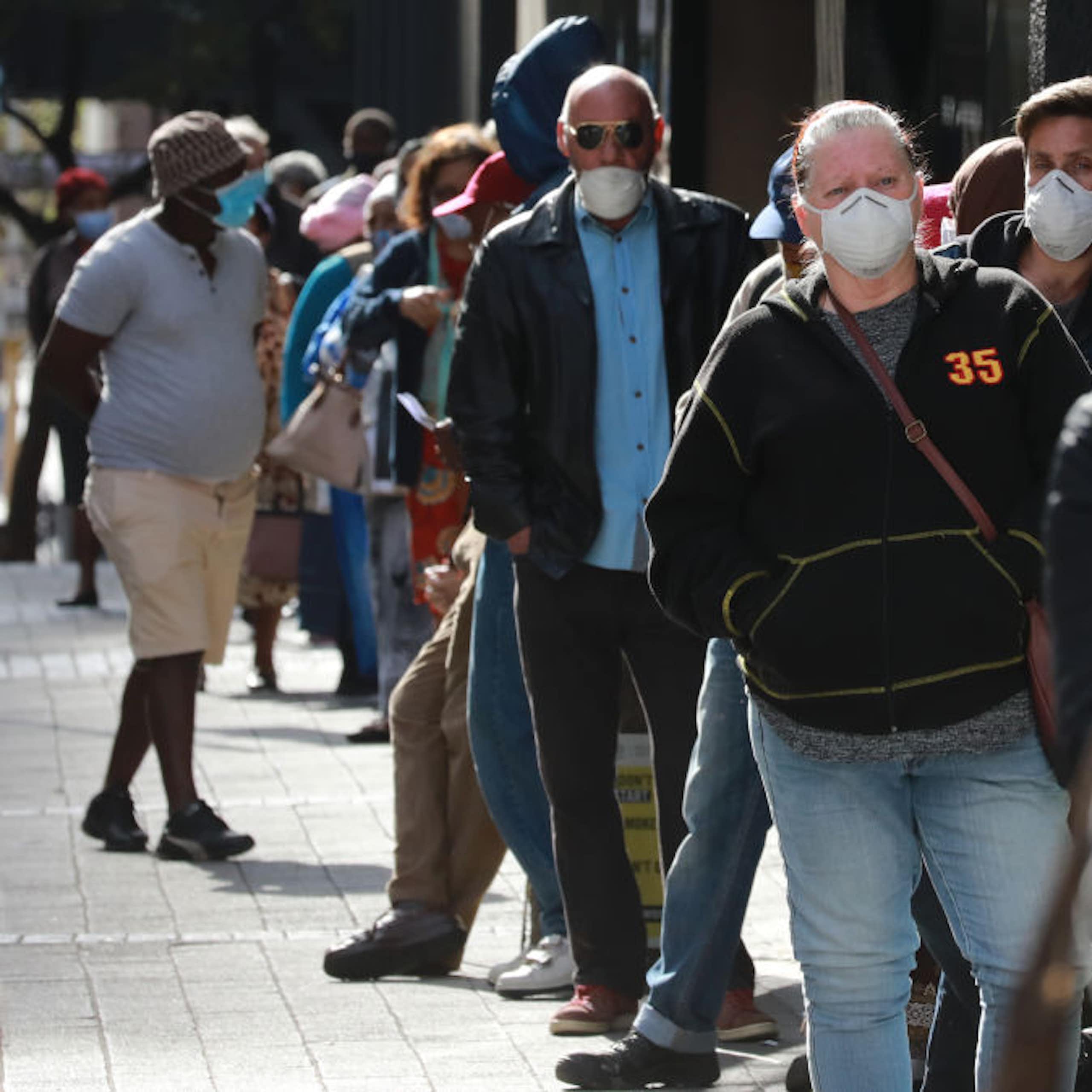 People standing outdoors in a queue, wearing COVID face masks