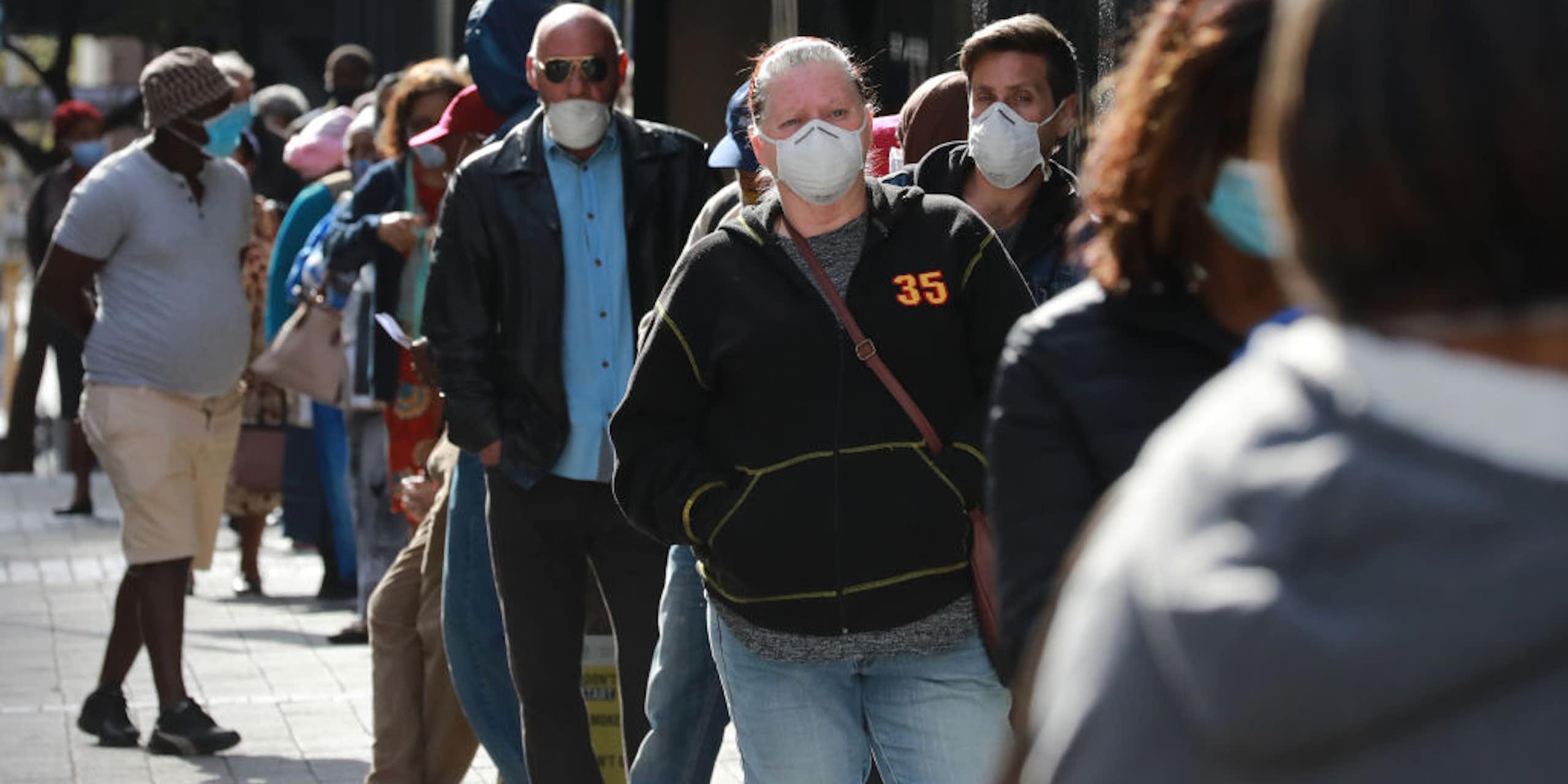 People standing outdoors in a queue, wearing COVID face masks