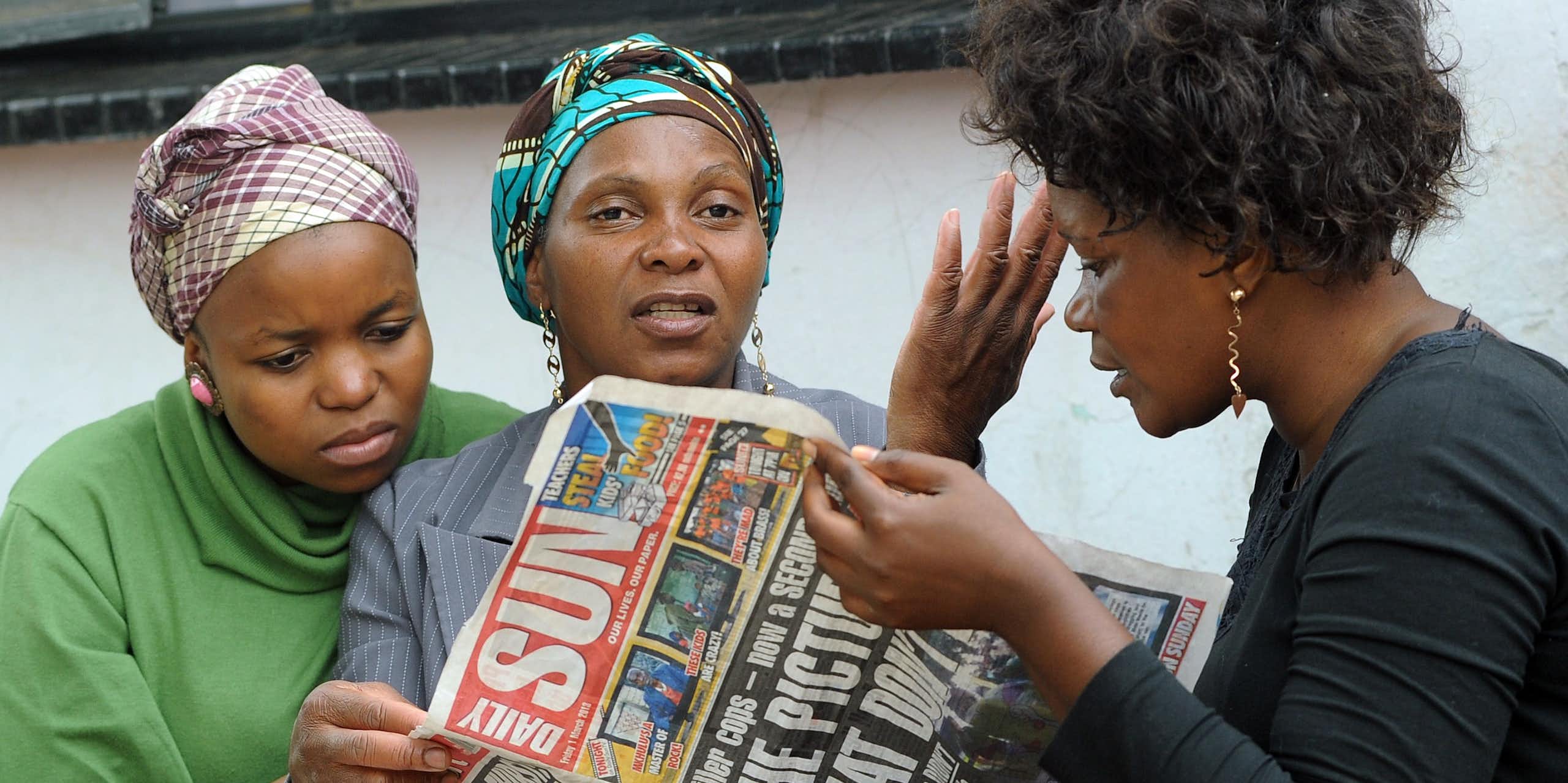 Three women read a copy of South Africa's Daily Sun newspaper. 