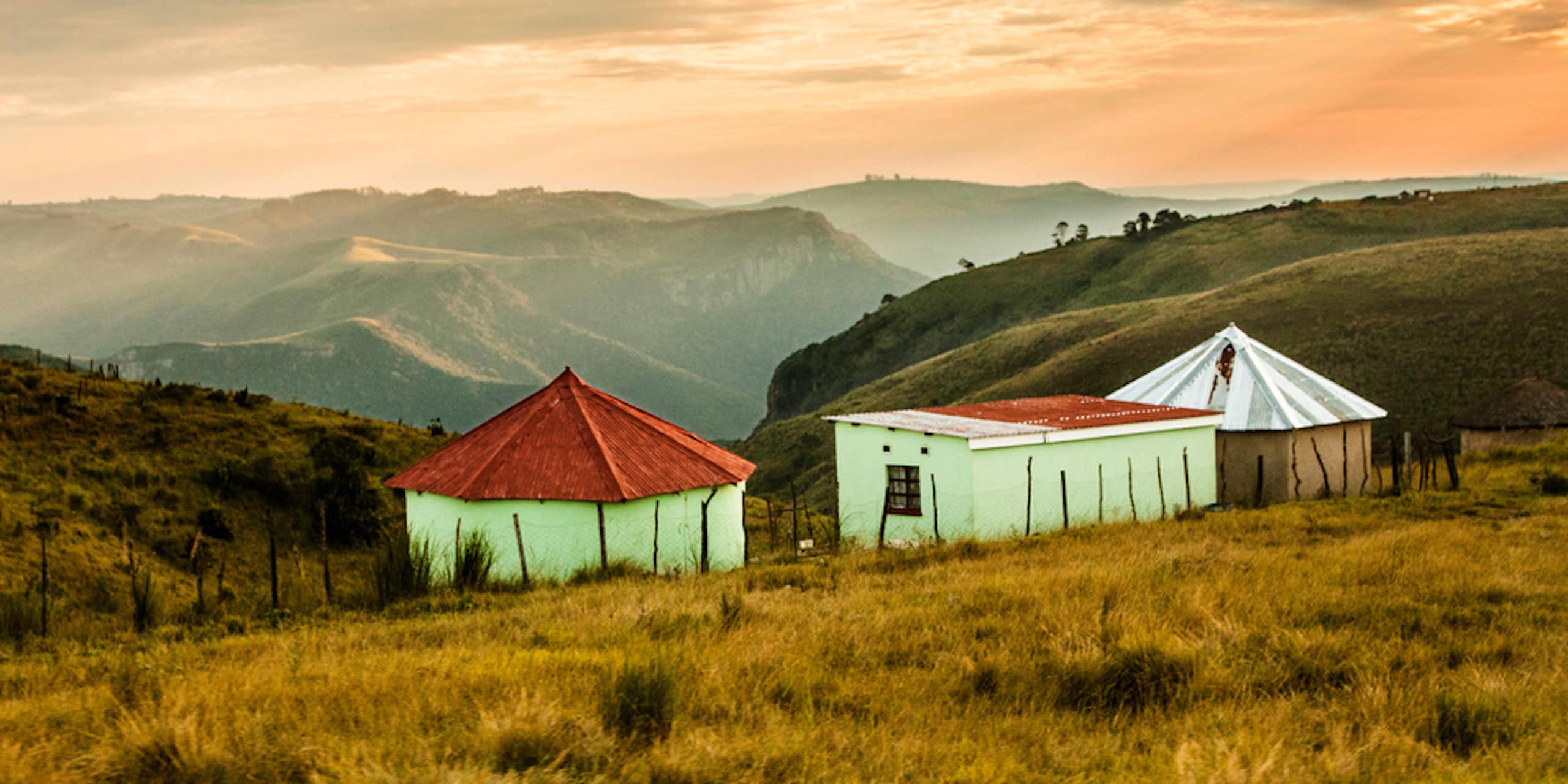 A landscape showing mountains and misty valleys, three huts in the foreground.