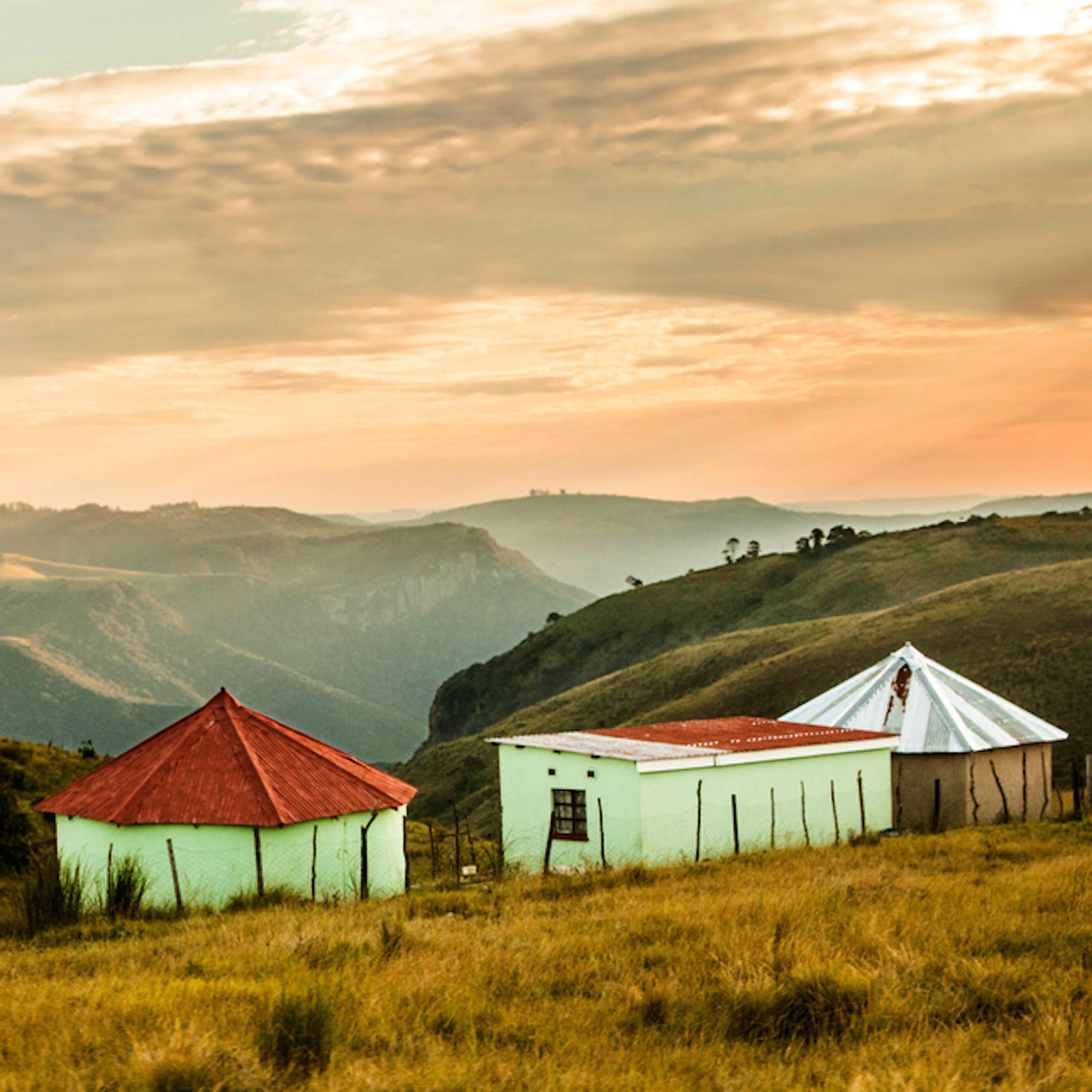 A landscape showing mountains and misty valleys, three huts in the foreground.