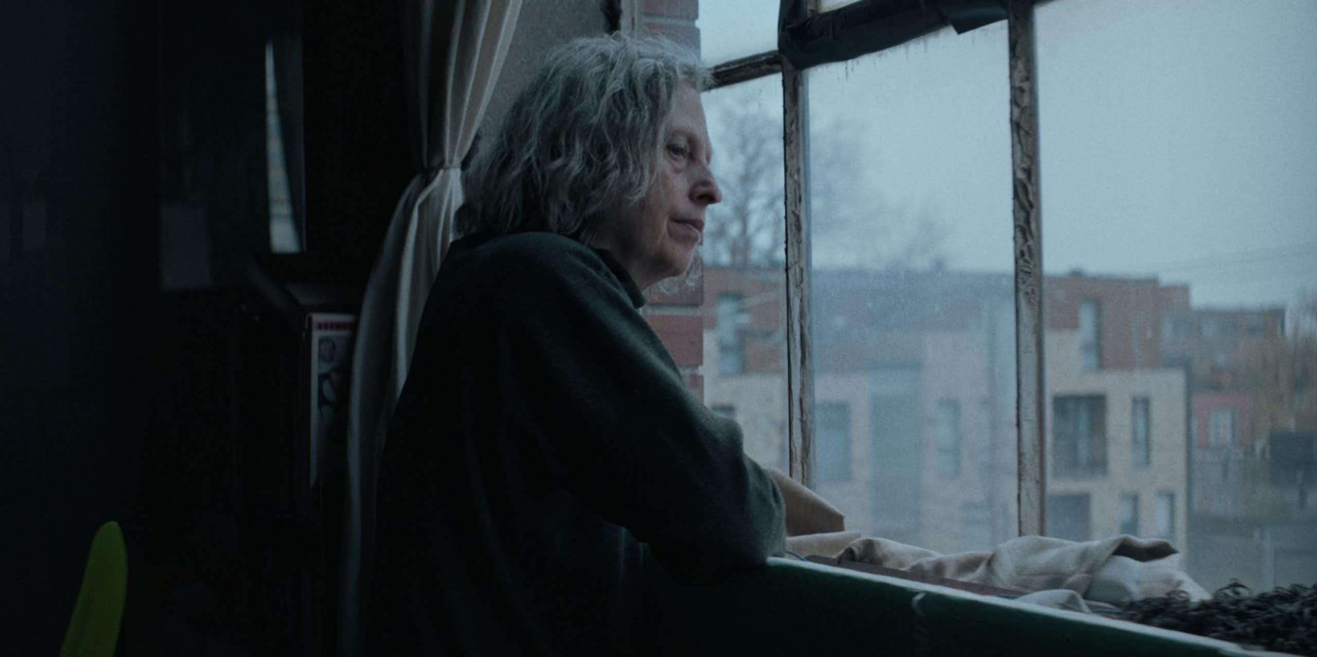 An elderly woman looks out of the window