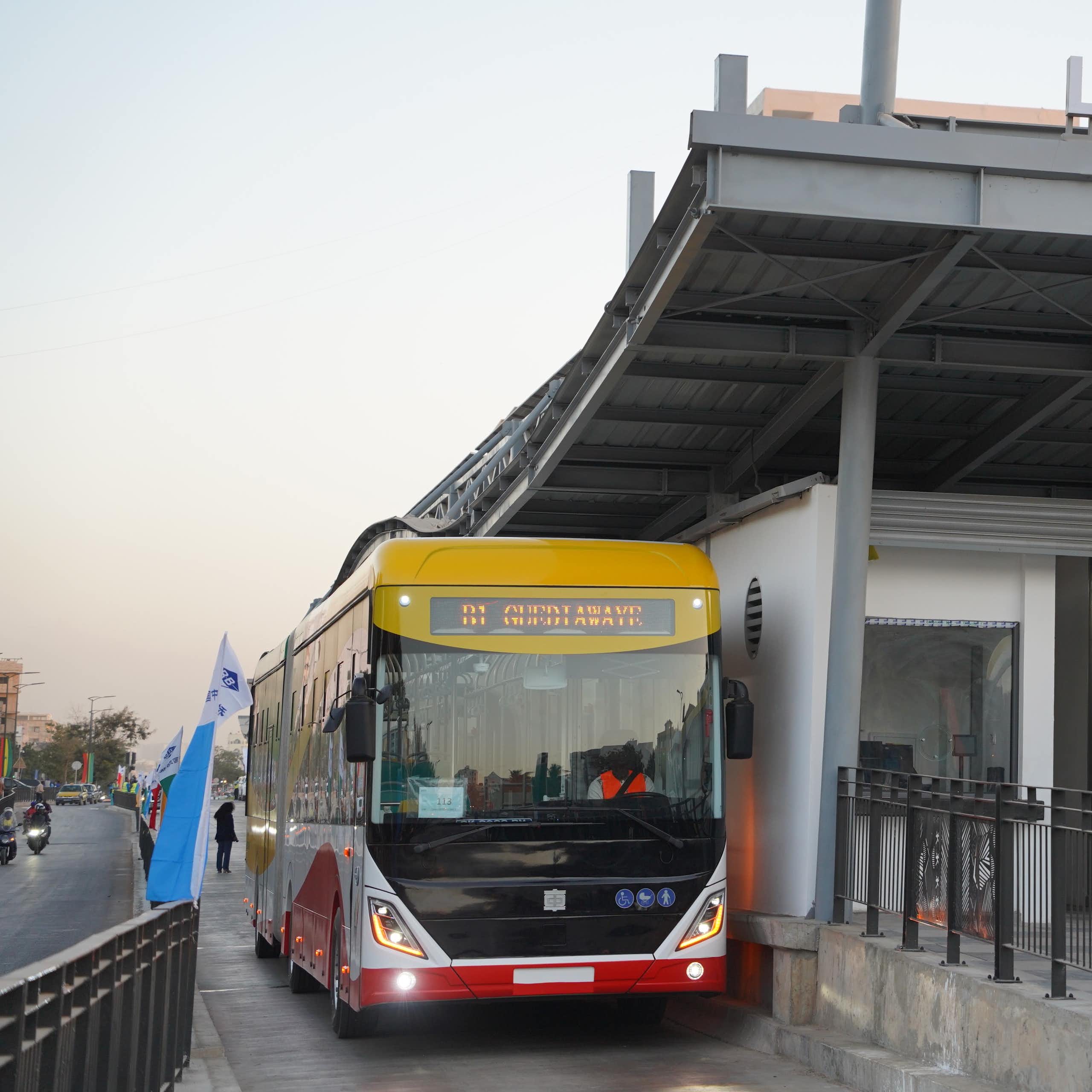 A red and yellow electric bus parked under a smart new bus shelter