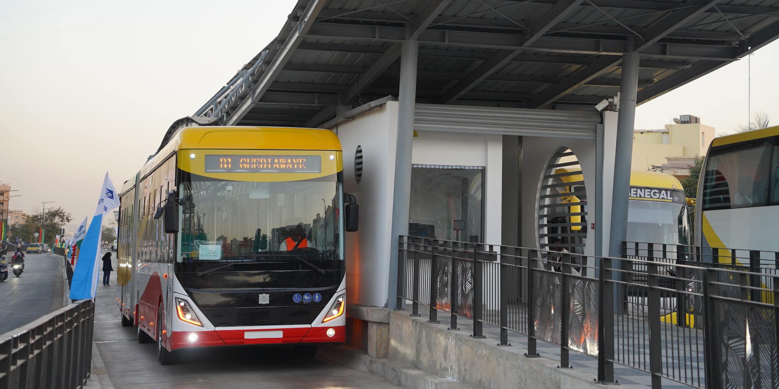 A red and yellow electric bus parked under a smart new bus shelter