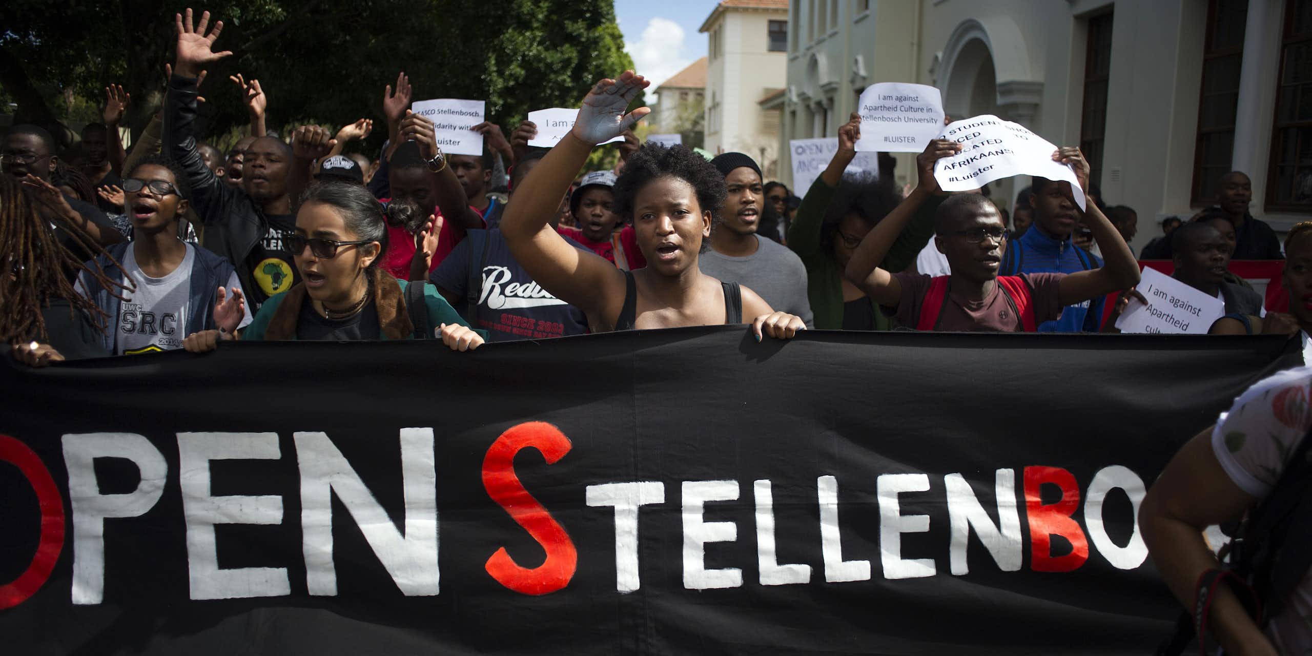 A group of protesters holding a banner that reads Open Stellenbosch. Others are holding placards calling for Afrikaans to be removed as a teaching language