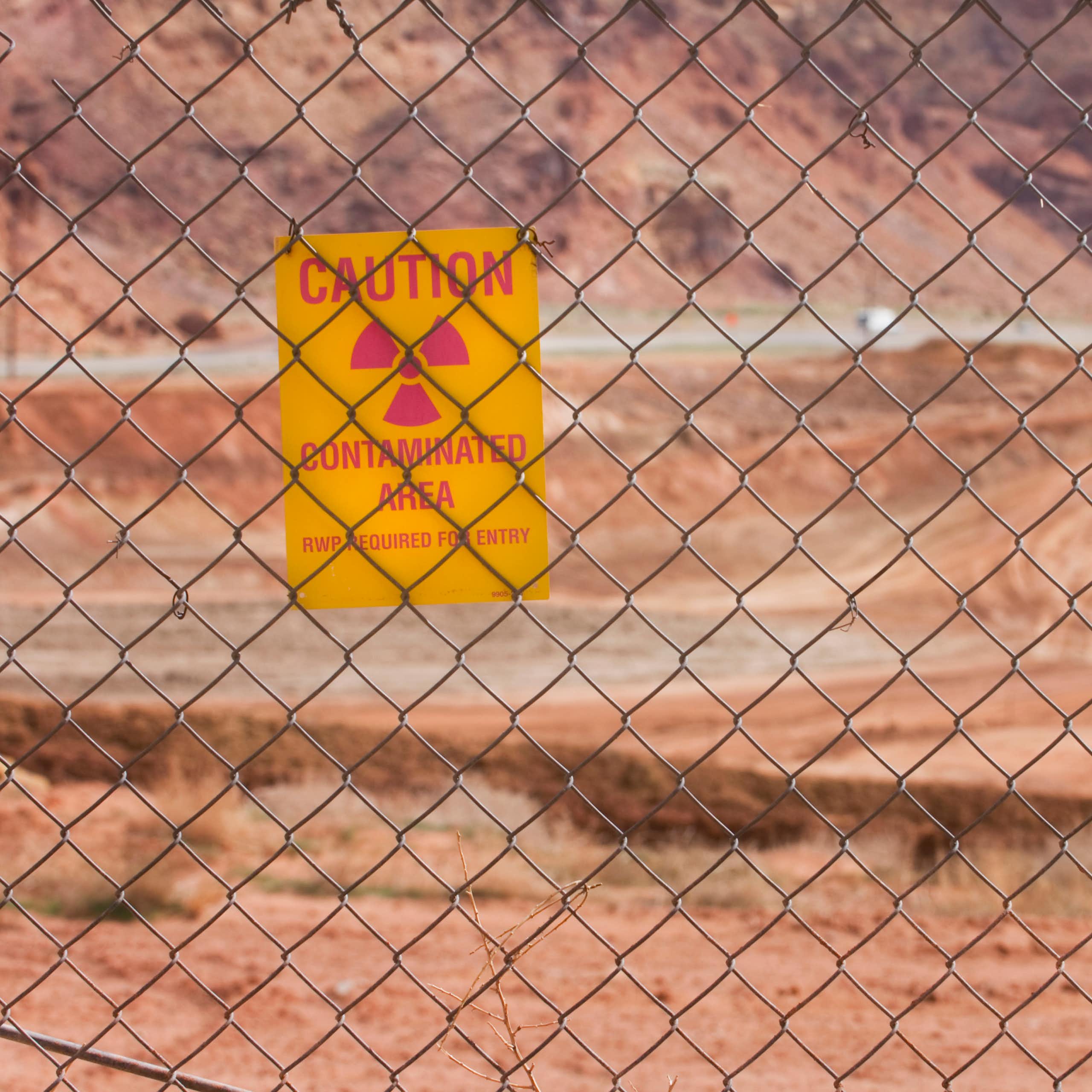 A big sandy area seen through a wire fence. Hanging on the fence is a notice - caution, contaminated area
