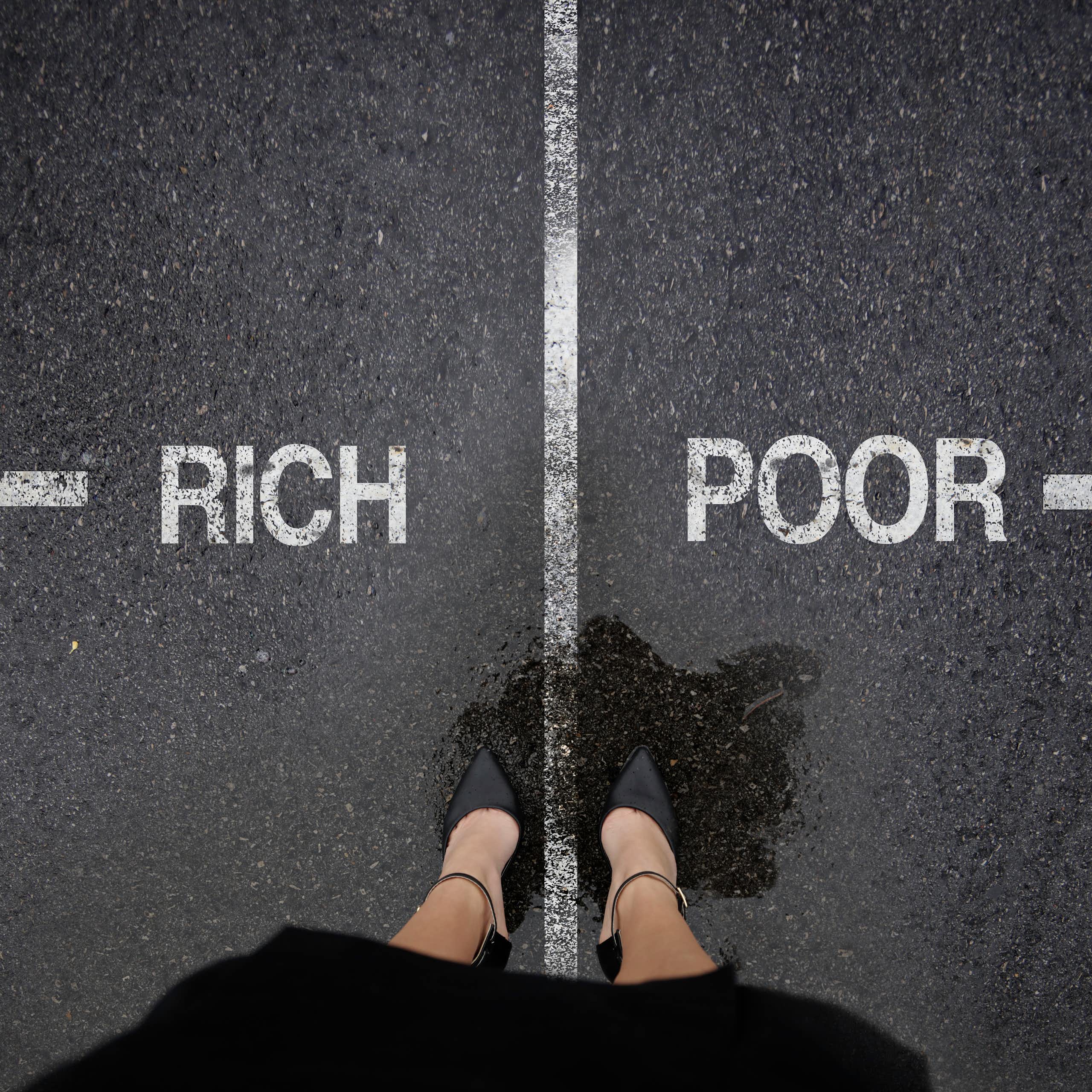 A woman stands at a painted divide in the road, with an arrow pointing left for the rich and an arrow pointing right for the poor.