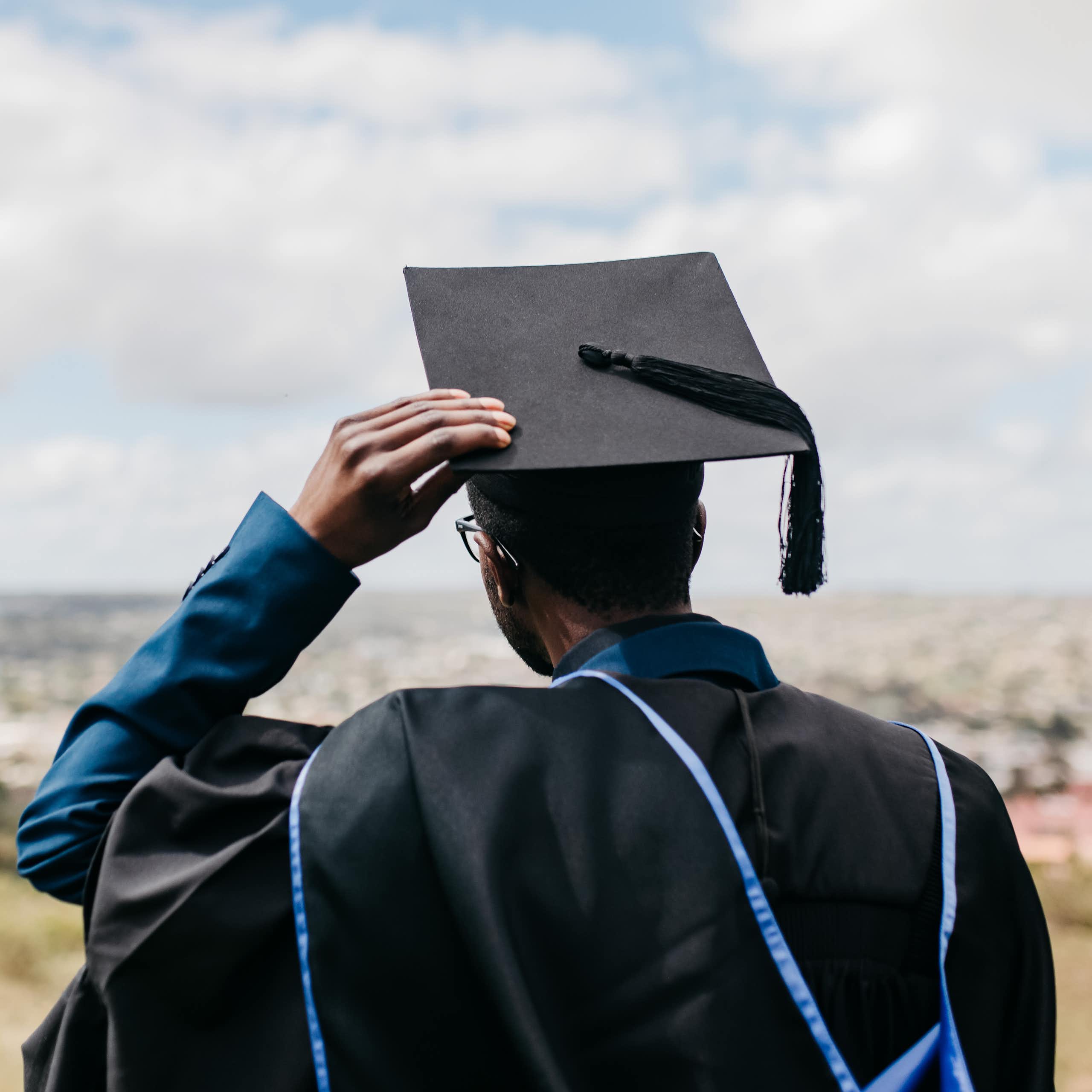 Rear view of male in academic gown, hood and cap, looking out over a distant landscape
