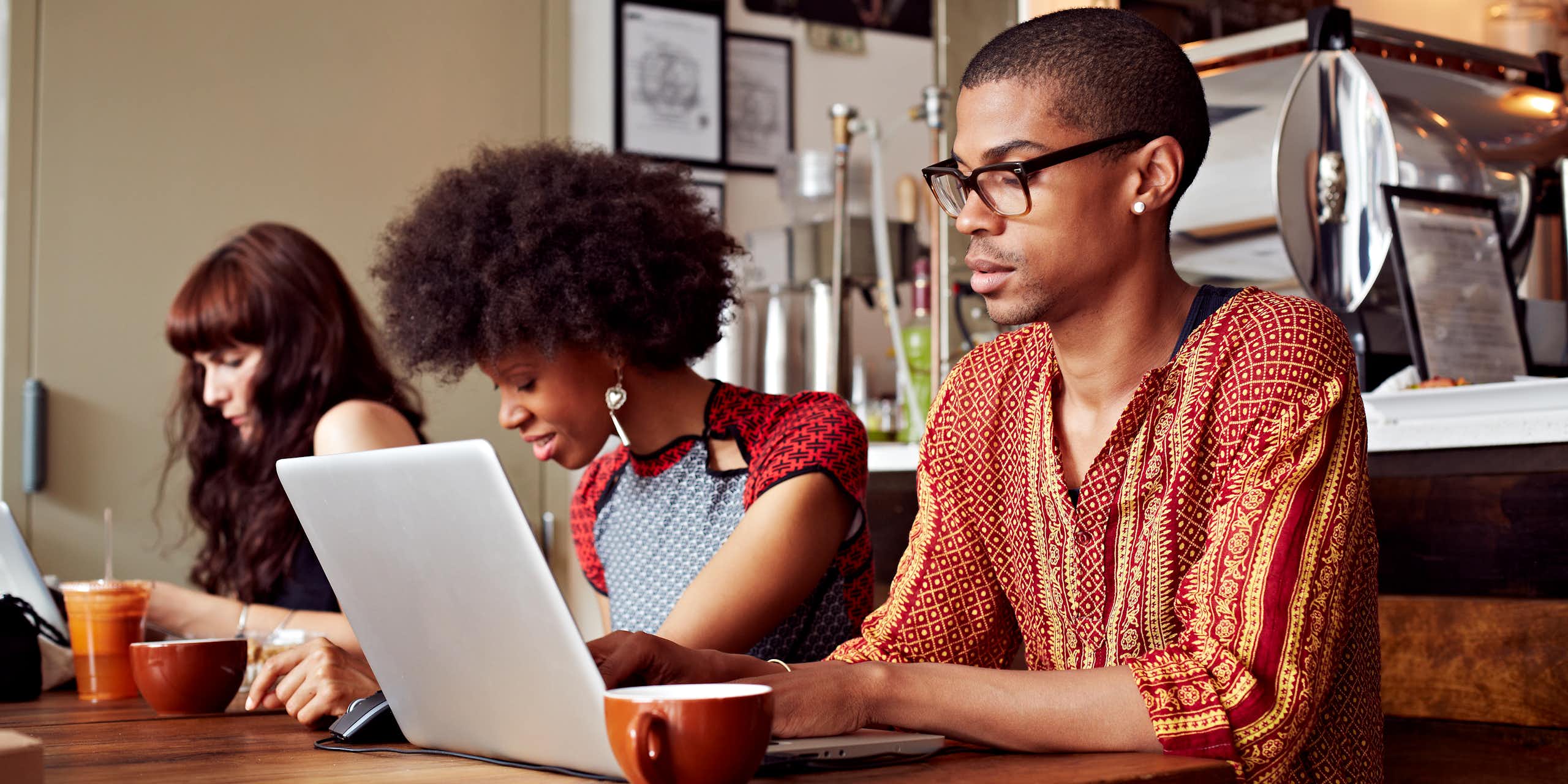 Three young people seated at a table with cups and a laptop