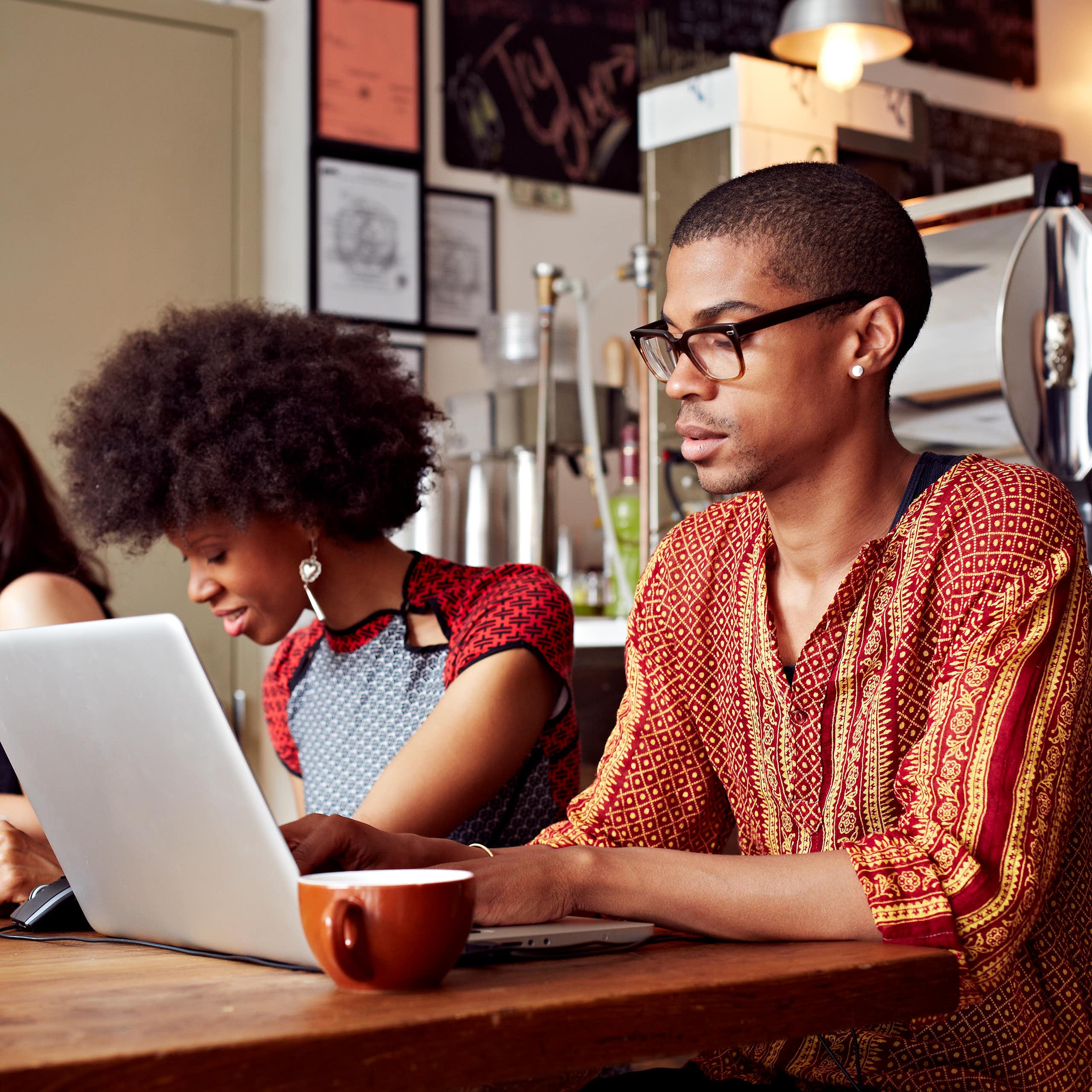 Three young people seated at a table with cups and a laptop