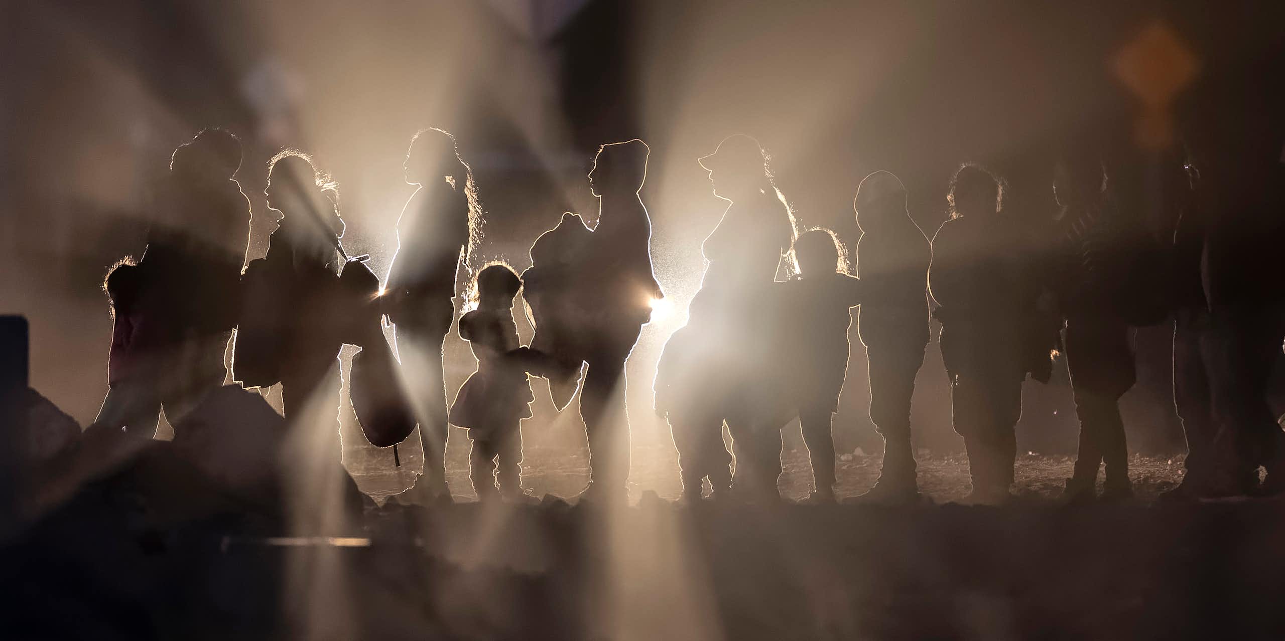 Immigrants, illuminated by car lights, form a line on the U.S.-Mexico border.