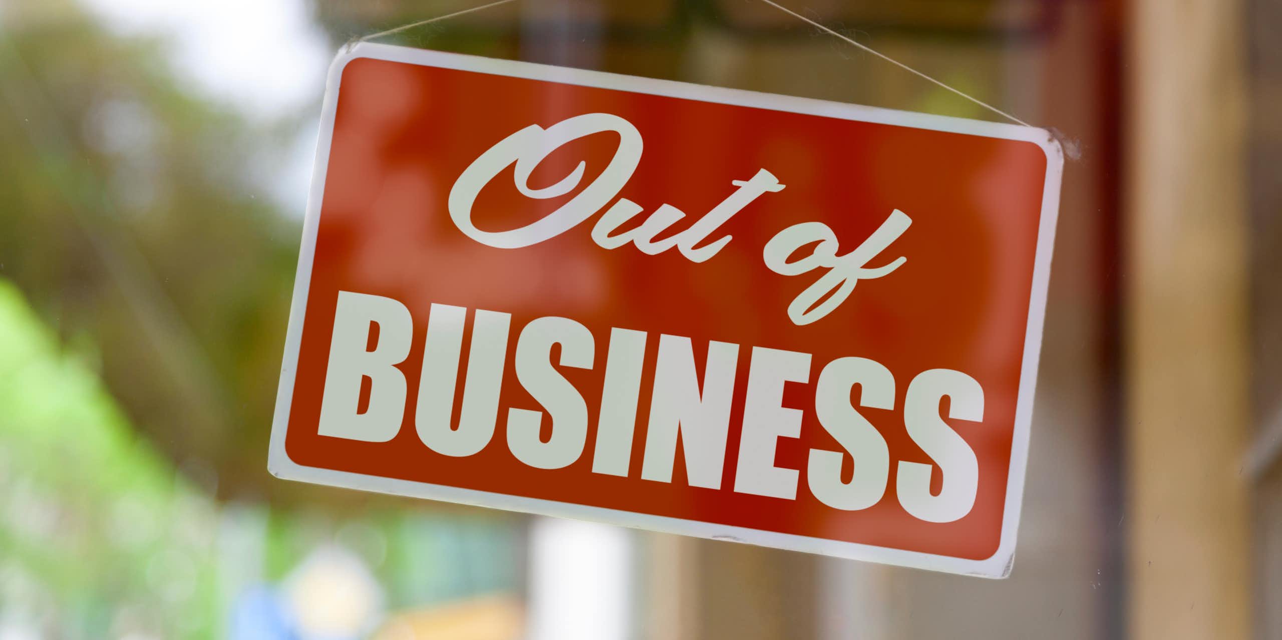 A sign that says 'Out of Business' hanging on the inside of a closed glass door