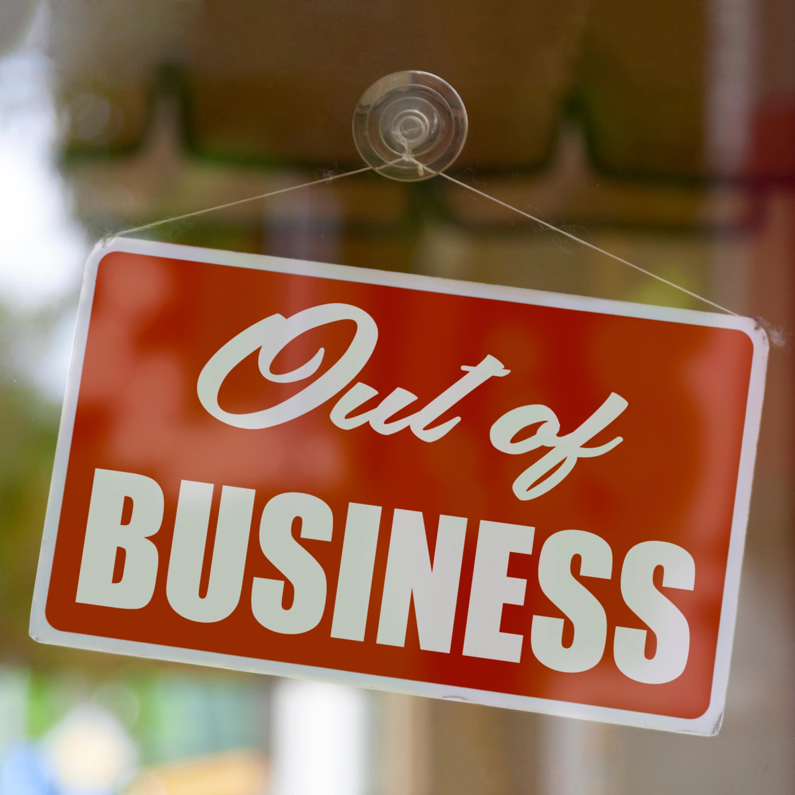 A sign that says 'Out of Business' hanging on the inside of a closed glass door