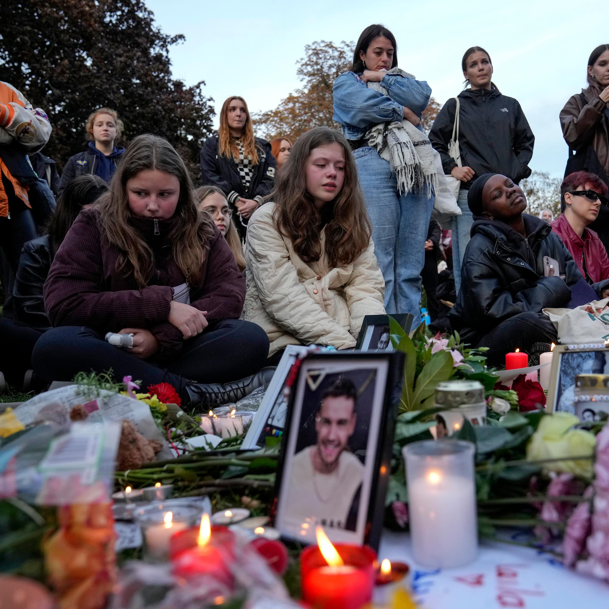 A group of young women stand and kneel next to a vigil with candles and photos of liam payne