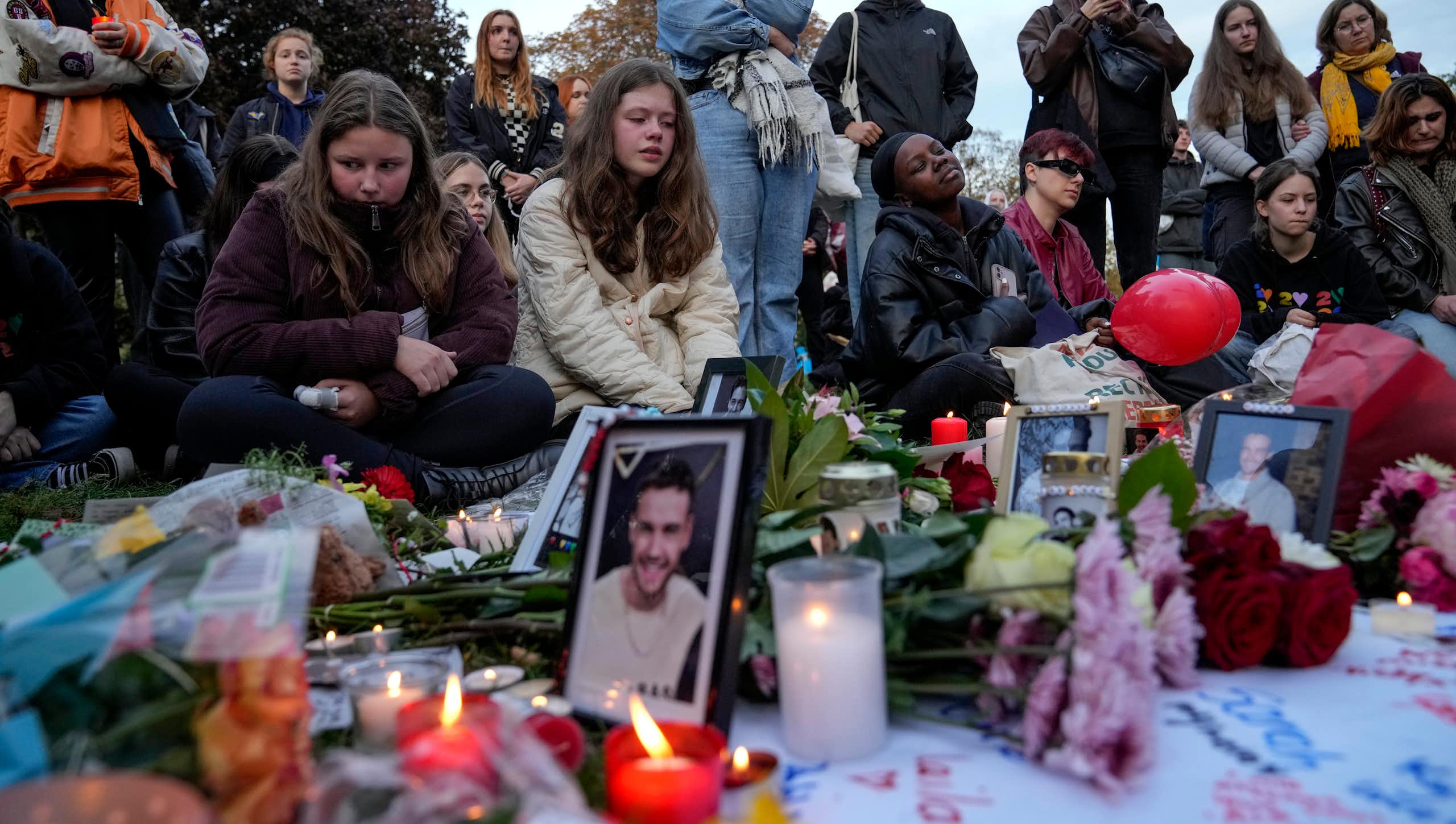 A group of young women stand and kneel next to a vigil with candles and photos of liam payne