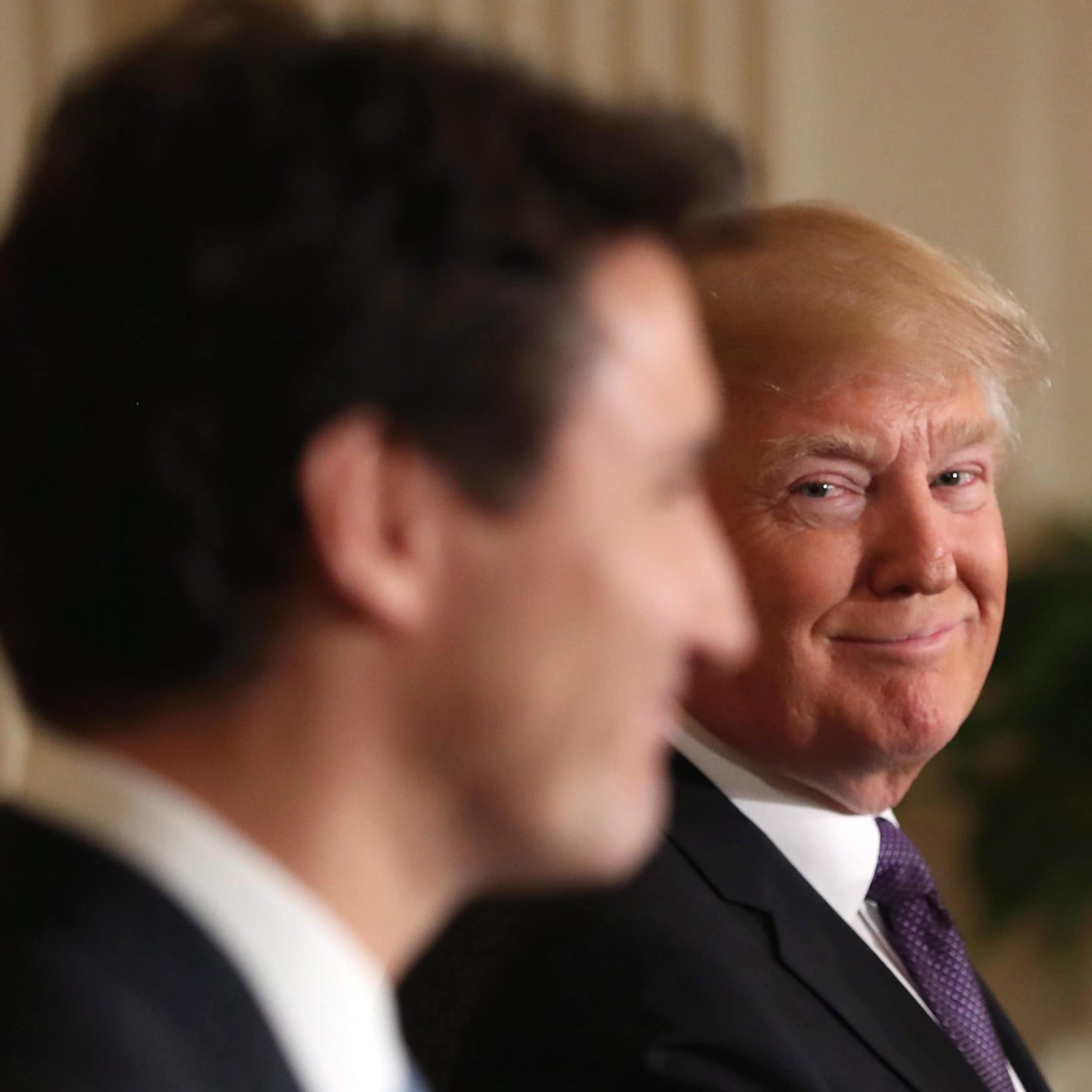 A man with orange-ish blond hair smiles over at a younger man with dark hair seen in silhouette.