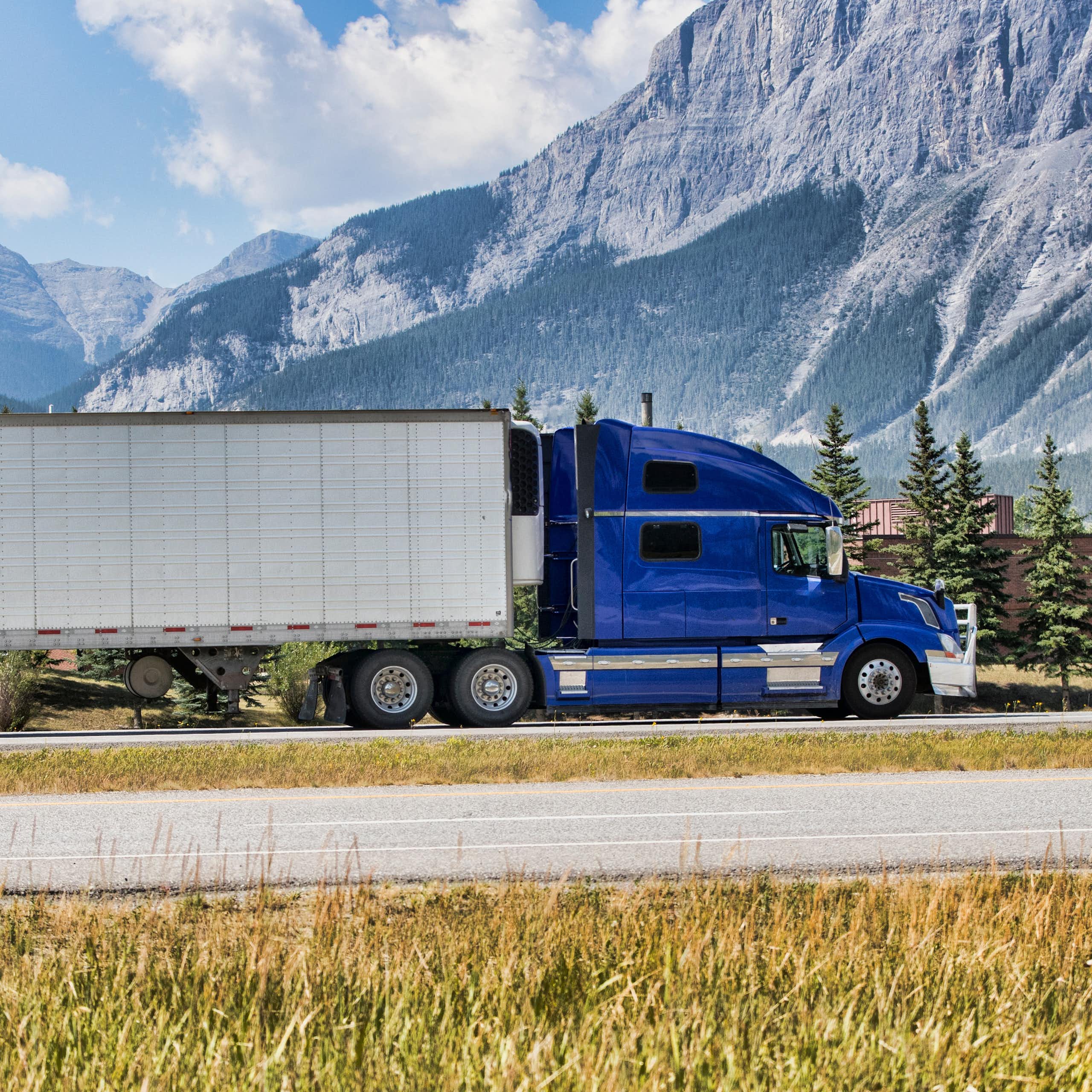 A transport truck with a bright-blue cab travels along a mountainous highway.