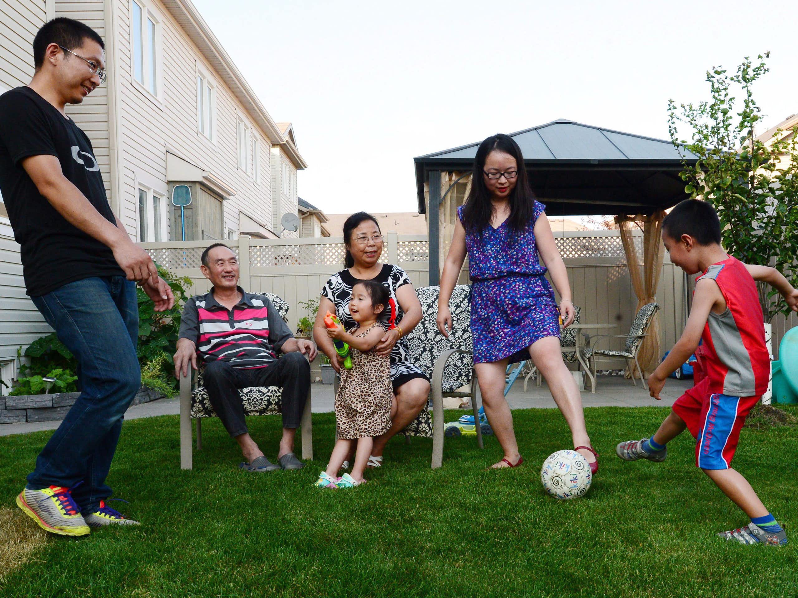 An asian family of parents, grandparents and small children play with a football in the backyard of a home