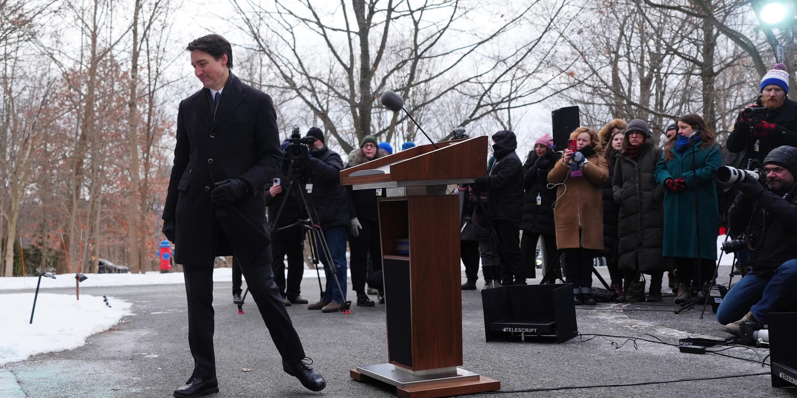 A smiling dark-haired man walks away from a media scrum.