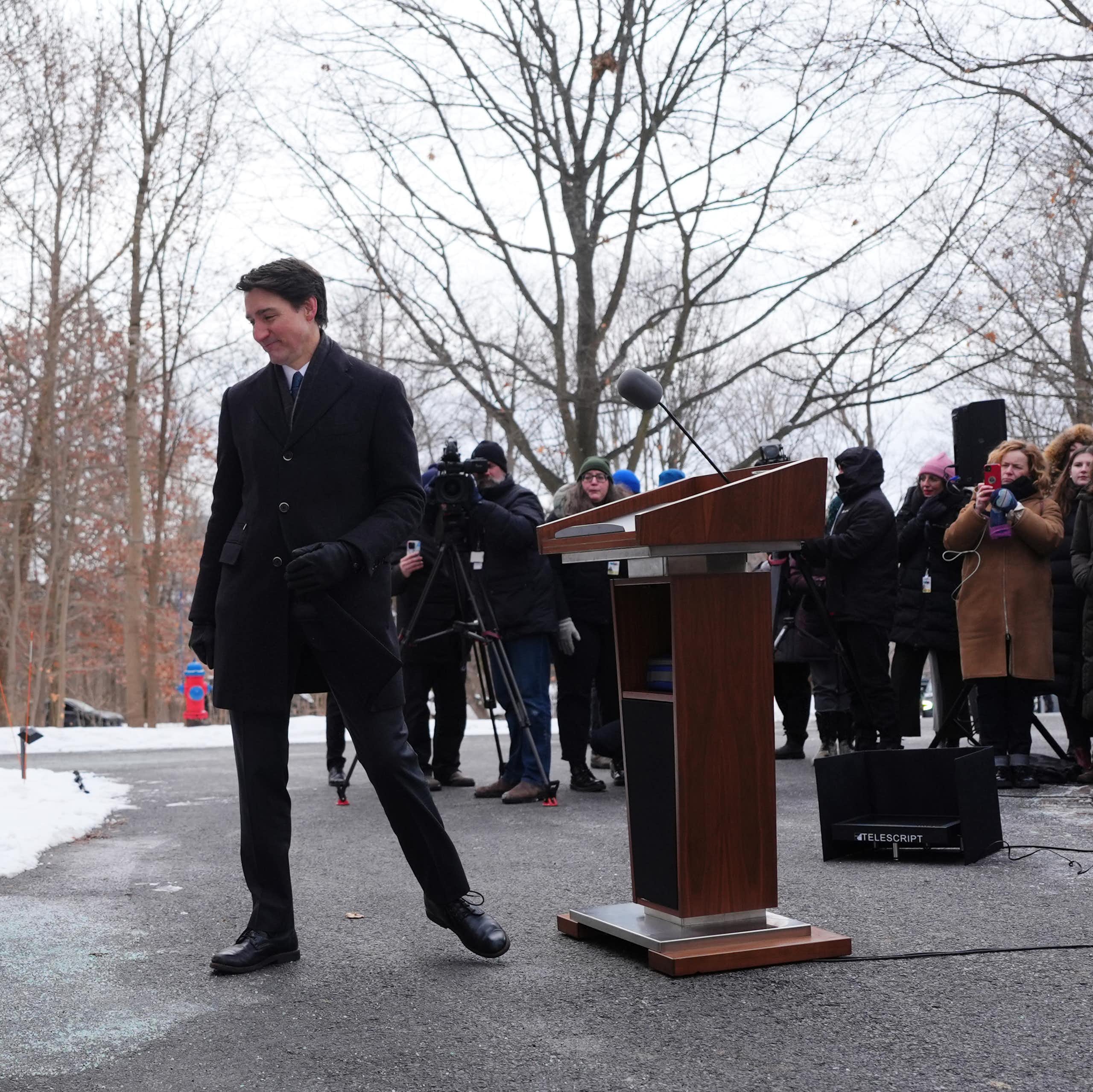 A smiling dark-haired man walks away from a media scrum.