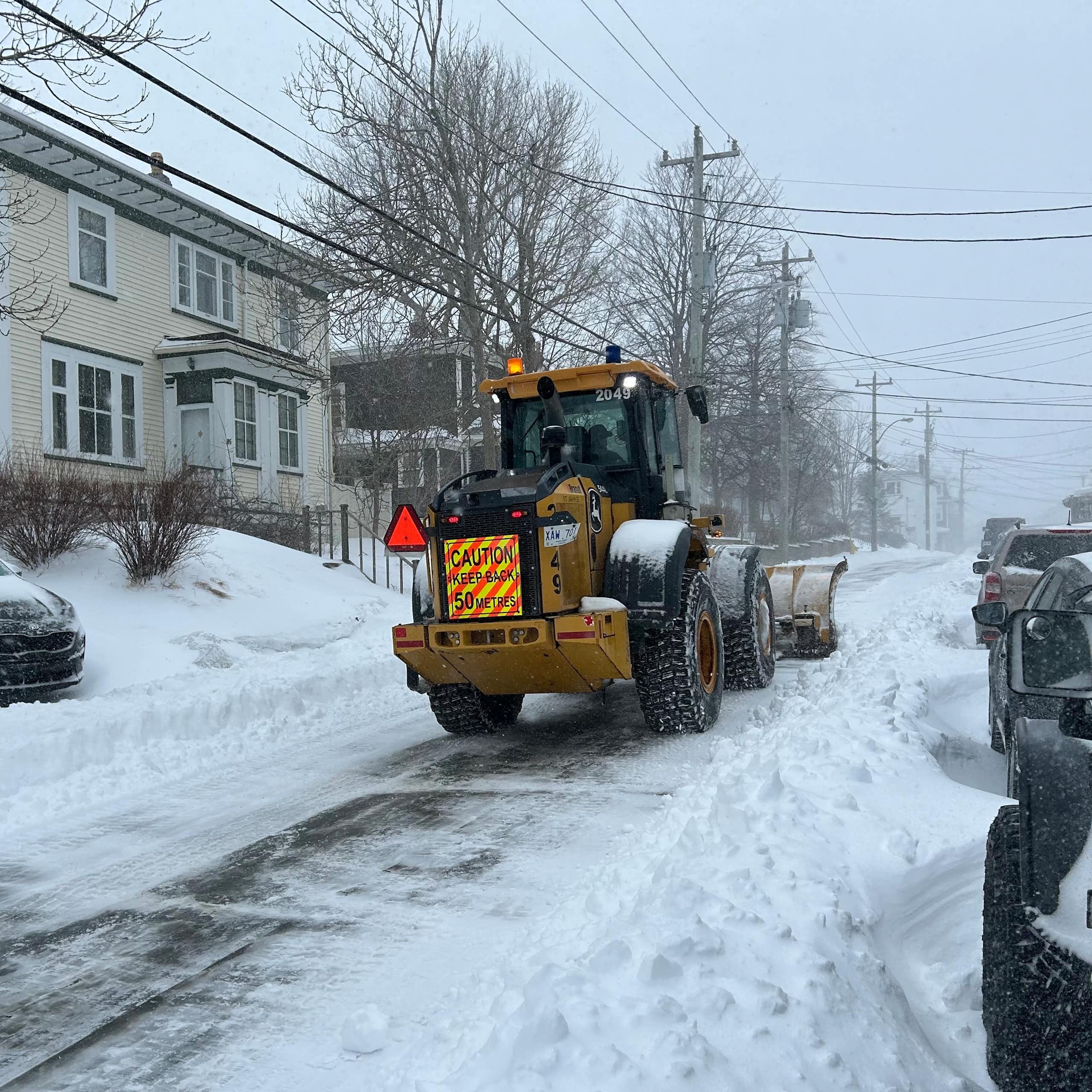 A snow plow drives down a snowy road.