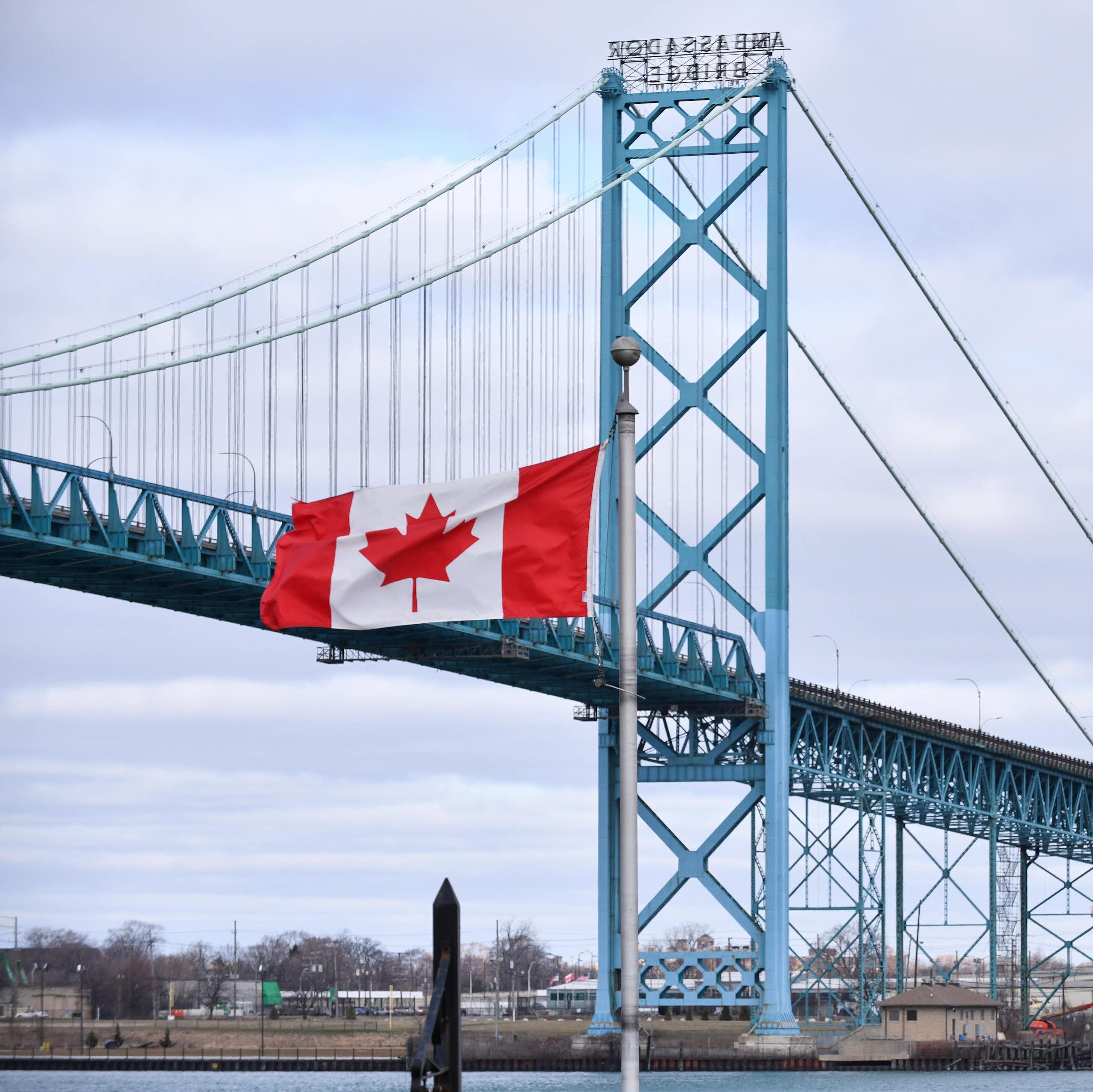 A Canadian flag and an American flag stand in front of a suspension bridge