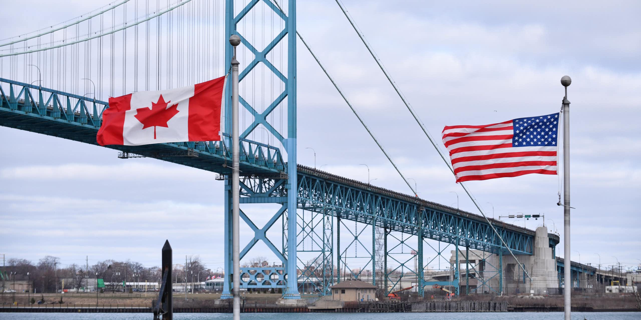 A Canadian flag and an American flag stand in front of a suspension bridge