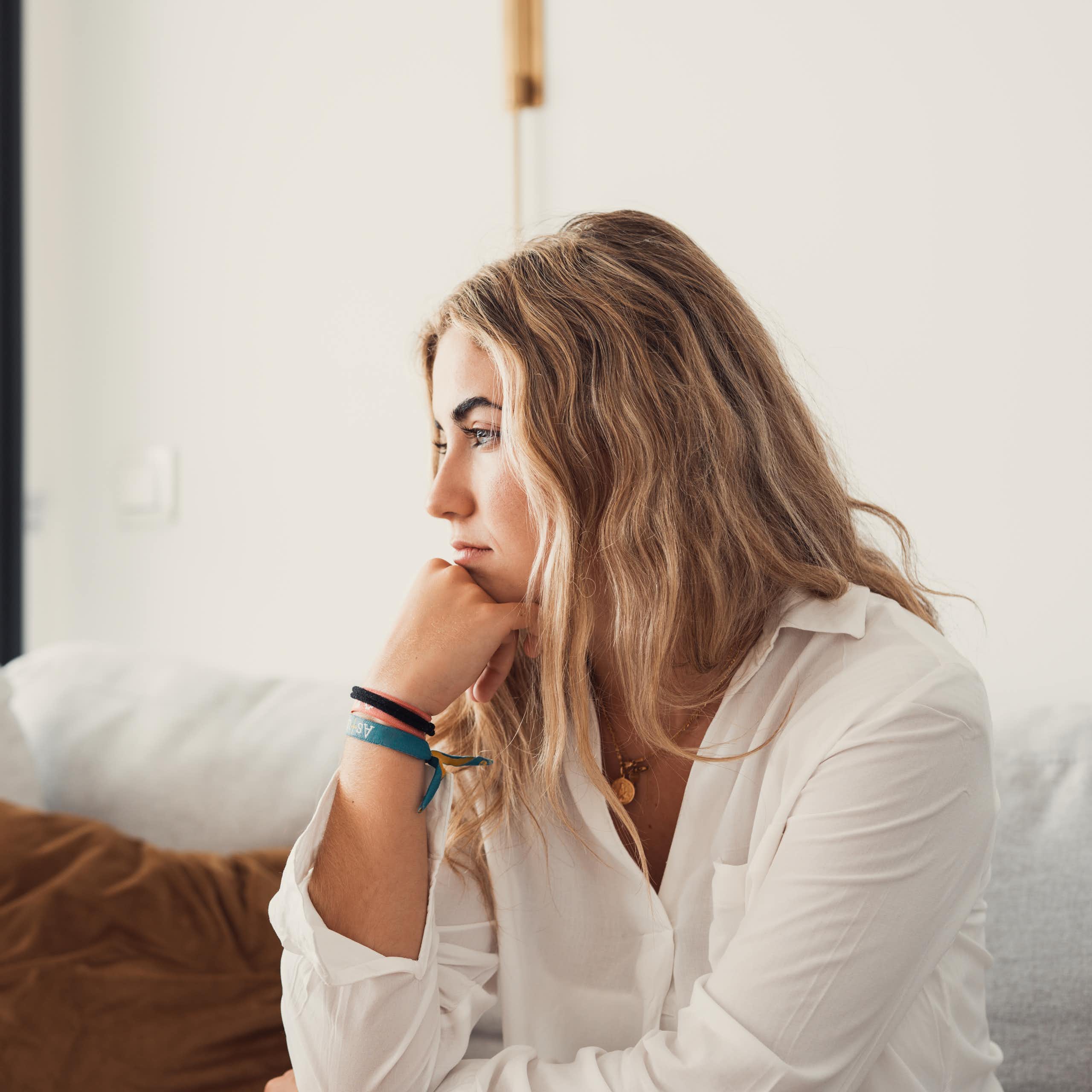 A woman sitting along on a couch with a contemplative expression.