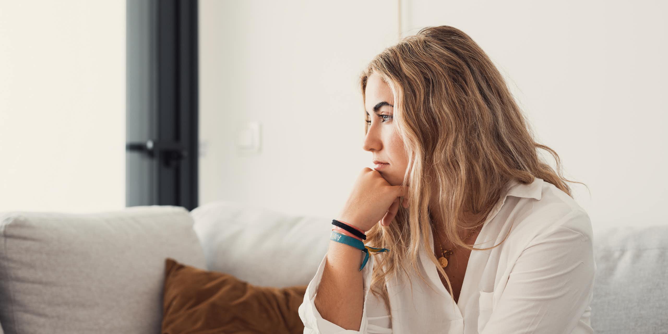 A woman sitting along on a couch with a contemplative expression.