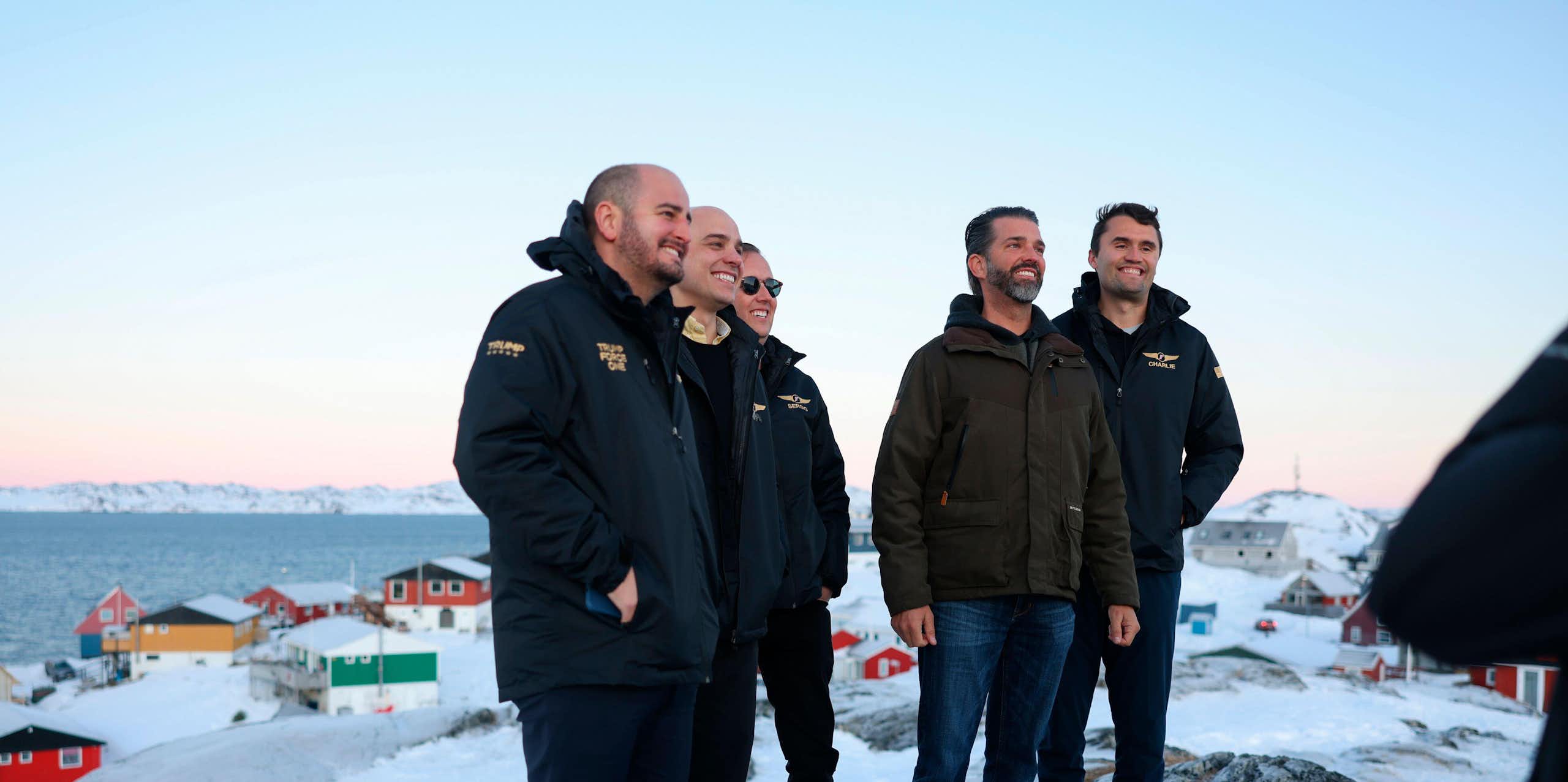 Donald Trump Junior stands on a snowy ridge with men in jackets in Greenland.