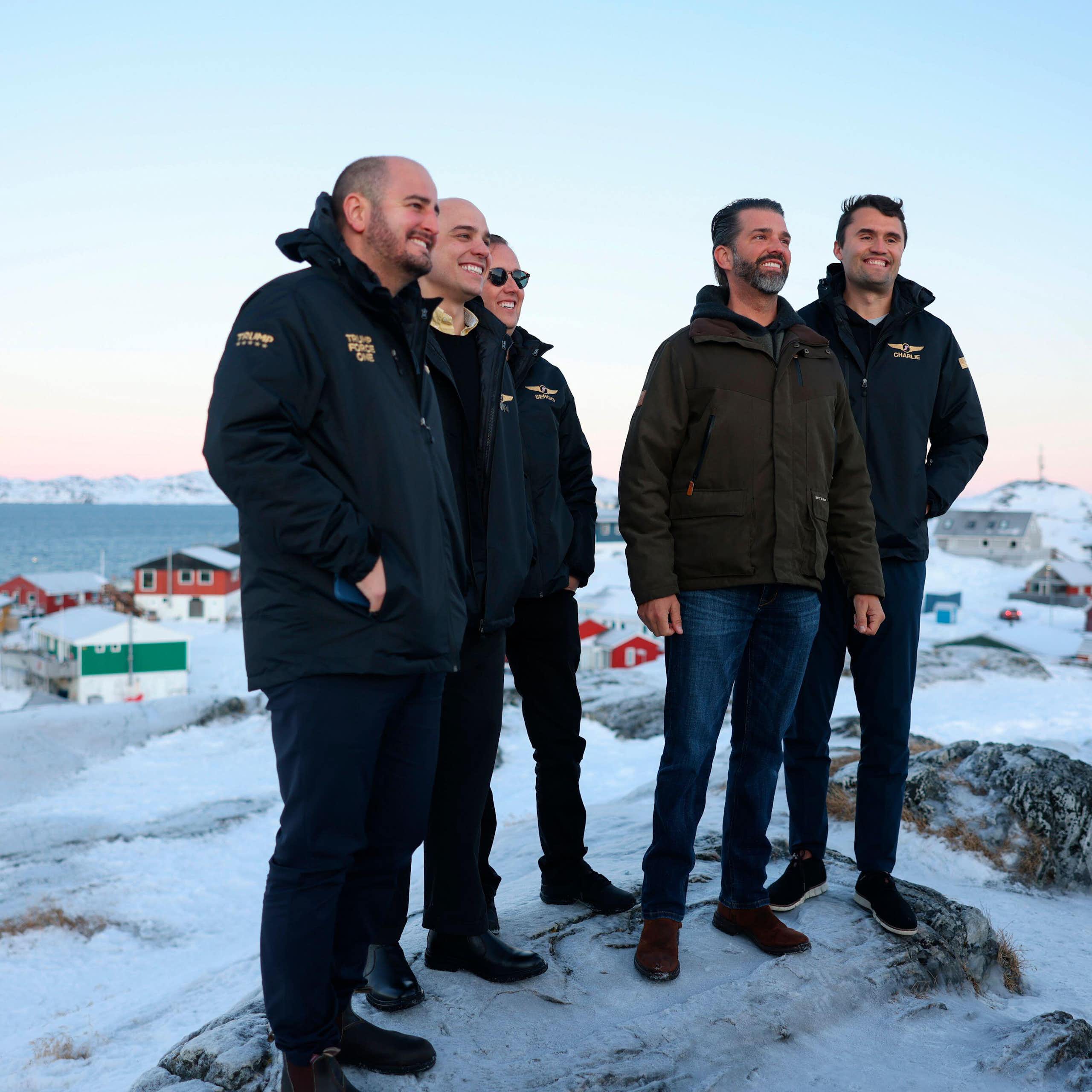 Donald Trump Junior stands on a snowy ridge with men in jackets in Greenland.