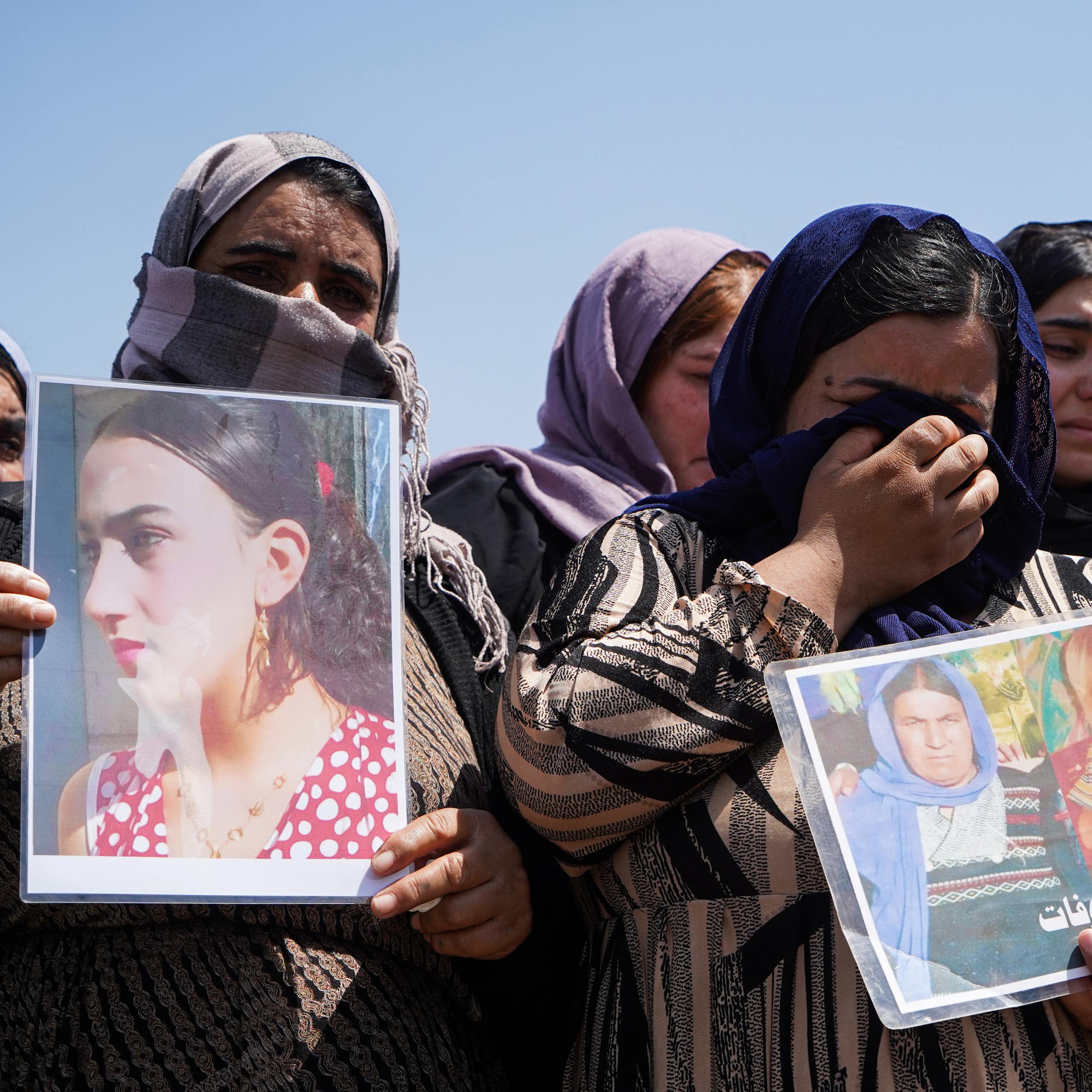Women in headscarves, many in tears, hold photos.