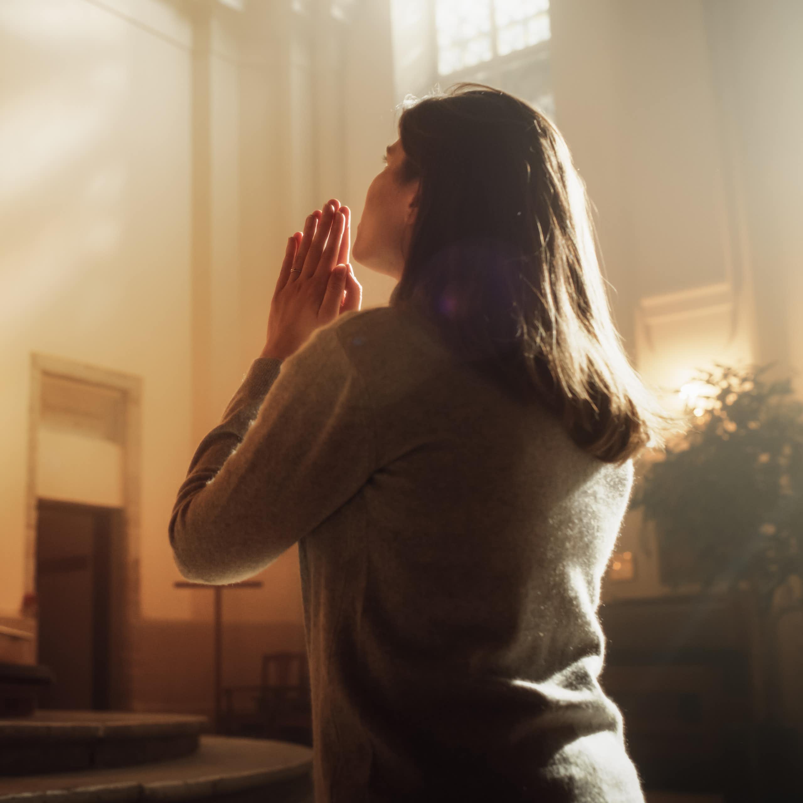 A woman in a church kneels and places her hands together in prayer.