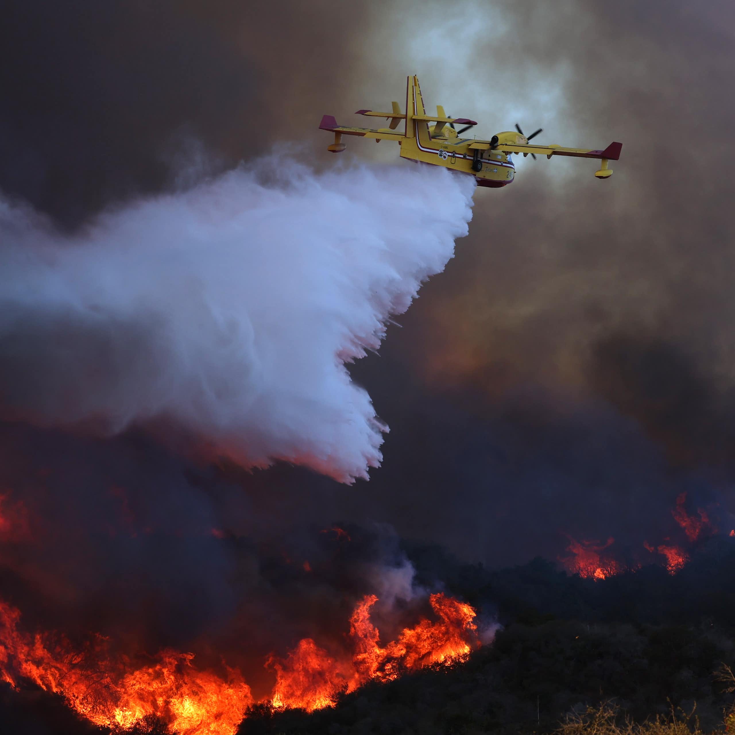 A plane dumps water onto a burning hillside