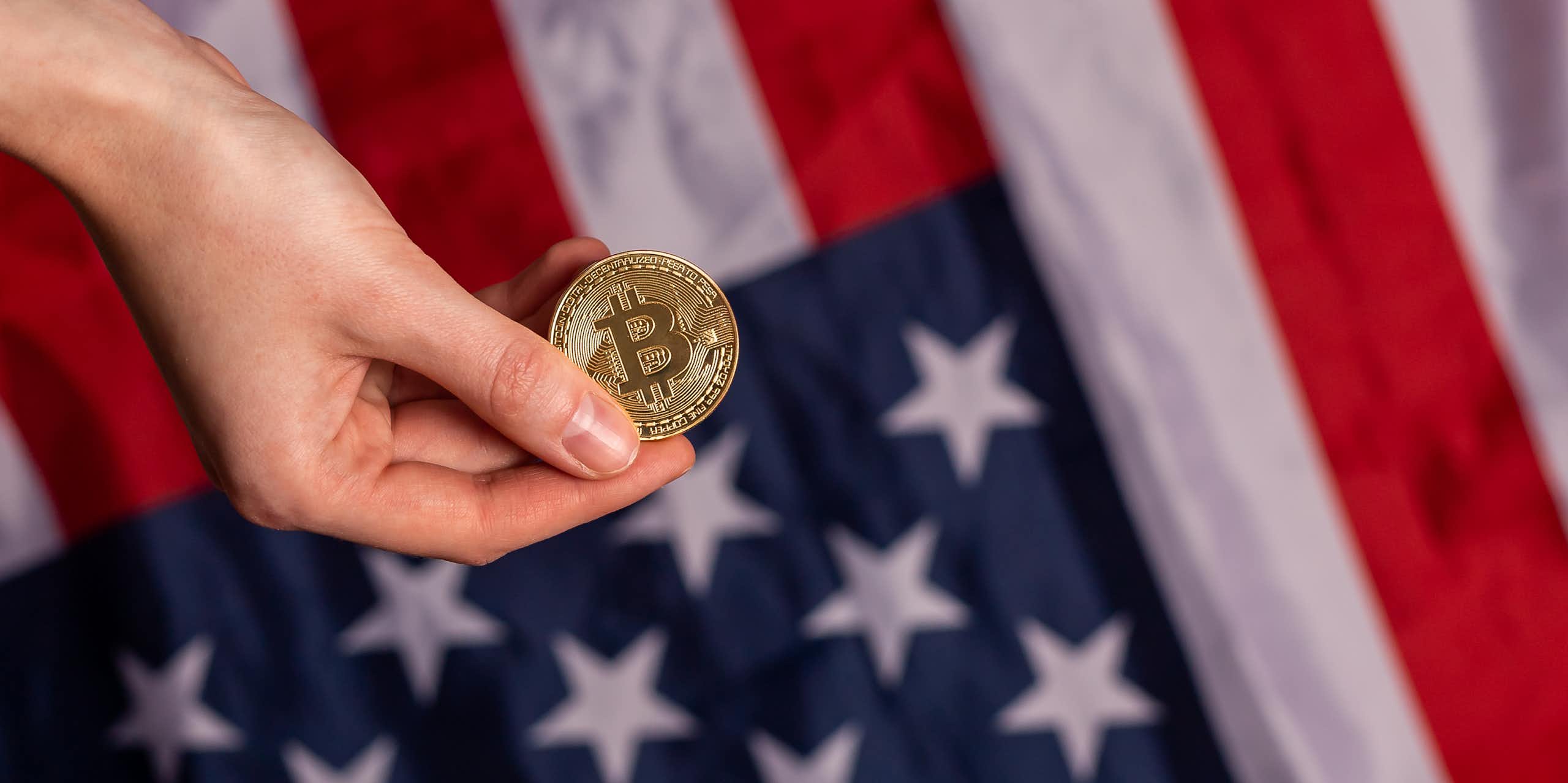 hand holding a representation of a bitcoin in front of the american flag