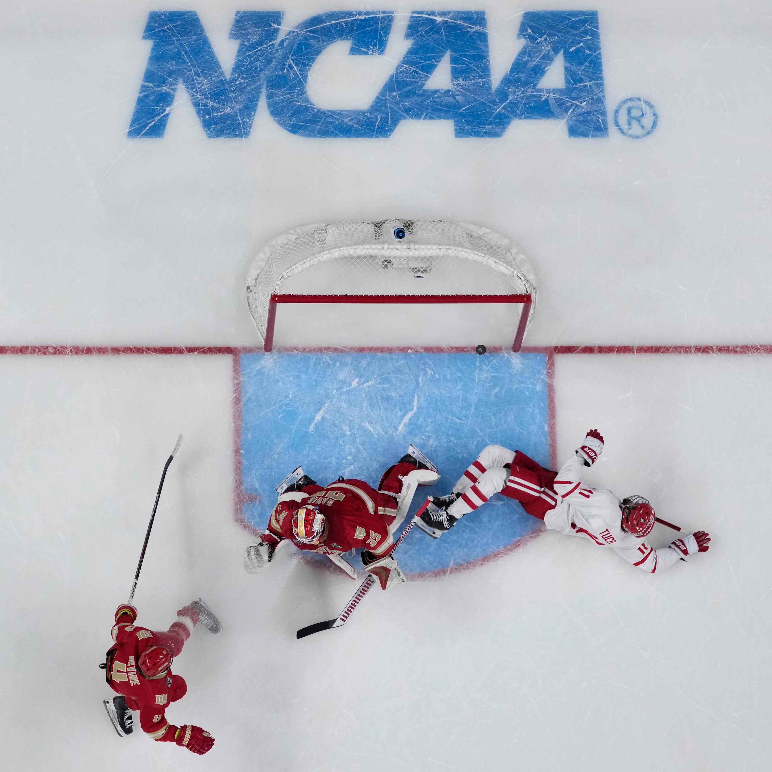 Overhead view of a hockey player in a white jersey scoring a goal against a goalie in a red jersey
