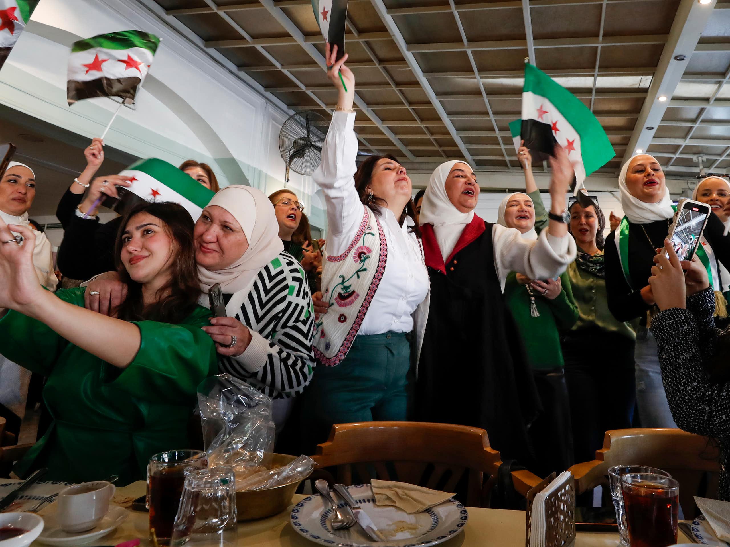 Un groupe de femmes sourit et fait la fête en brandissant des drapeaux syriens.