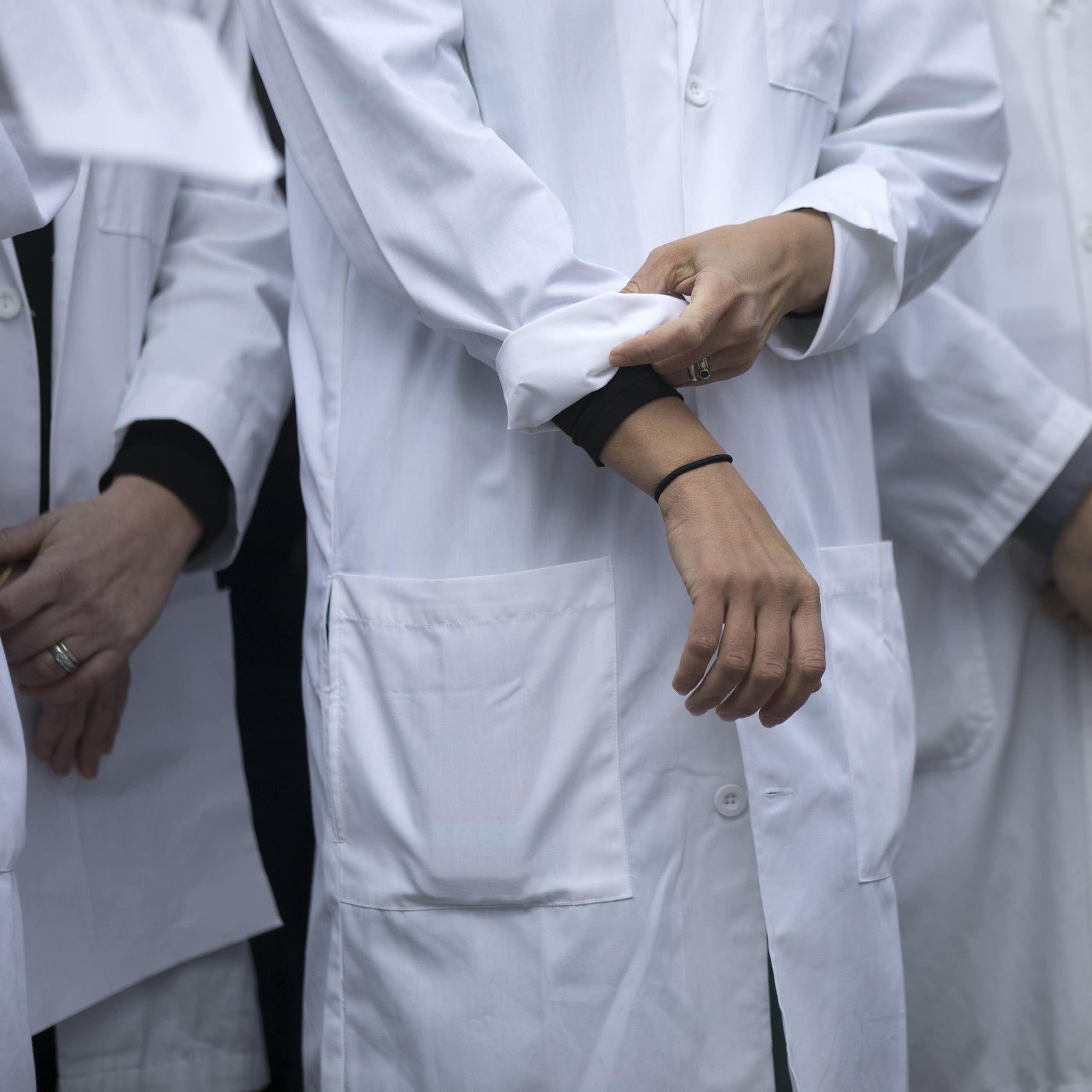 Close up of a doctor in white lab coat rolling up their sleeves