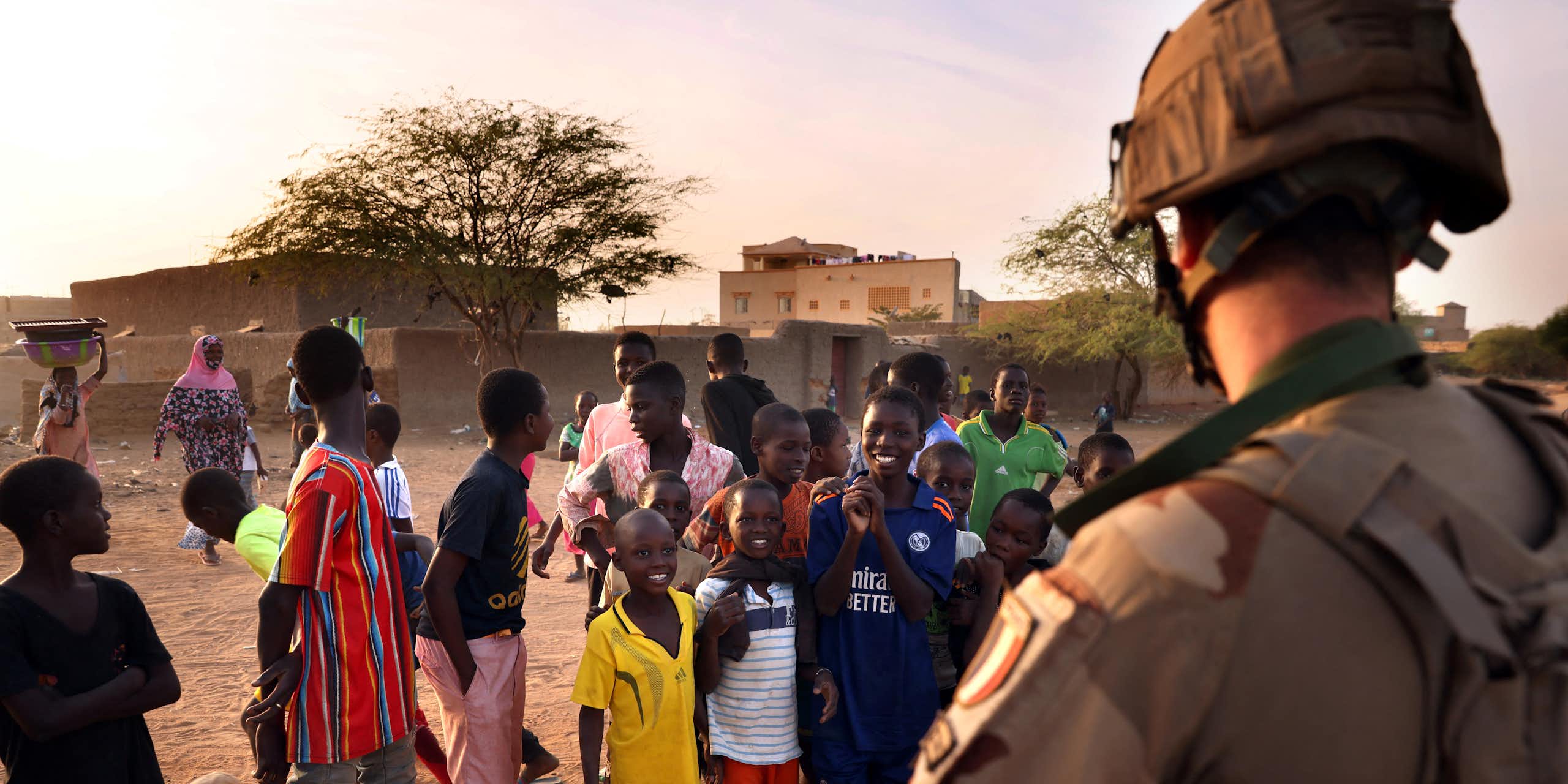 Children play soccer and stand looking at a man in military uniform