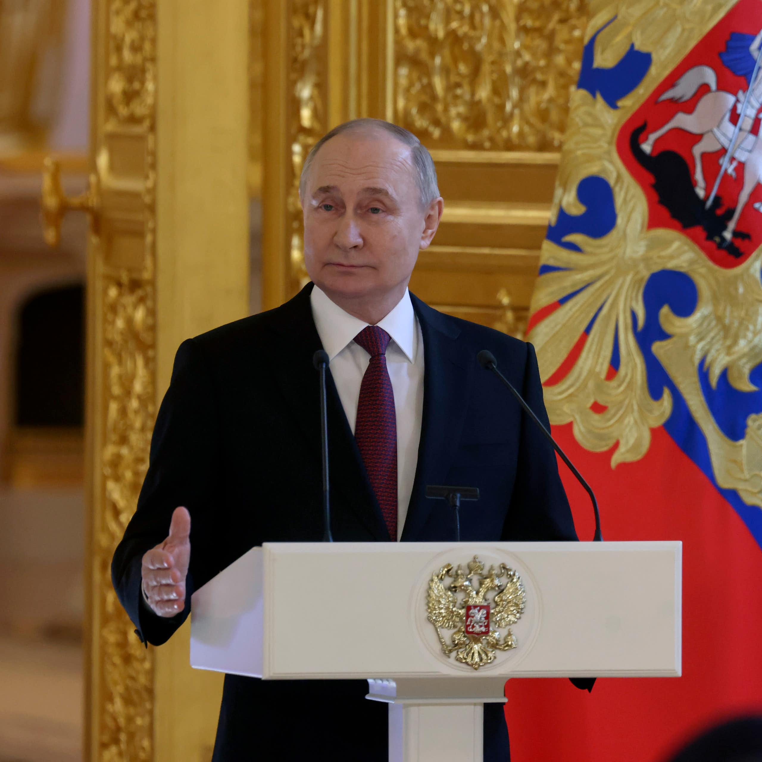 Vladimir Putin stands at a lectern flanked by a ceremonial guardsman.