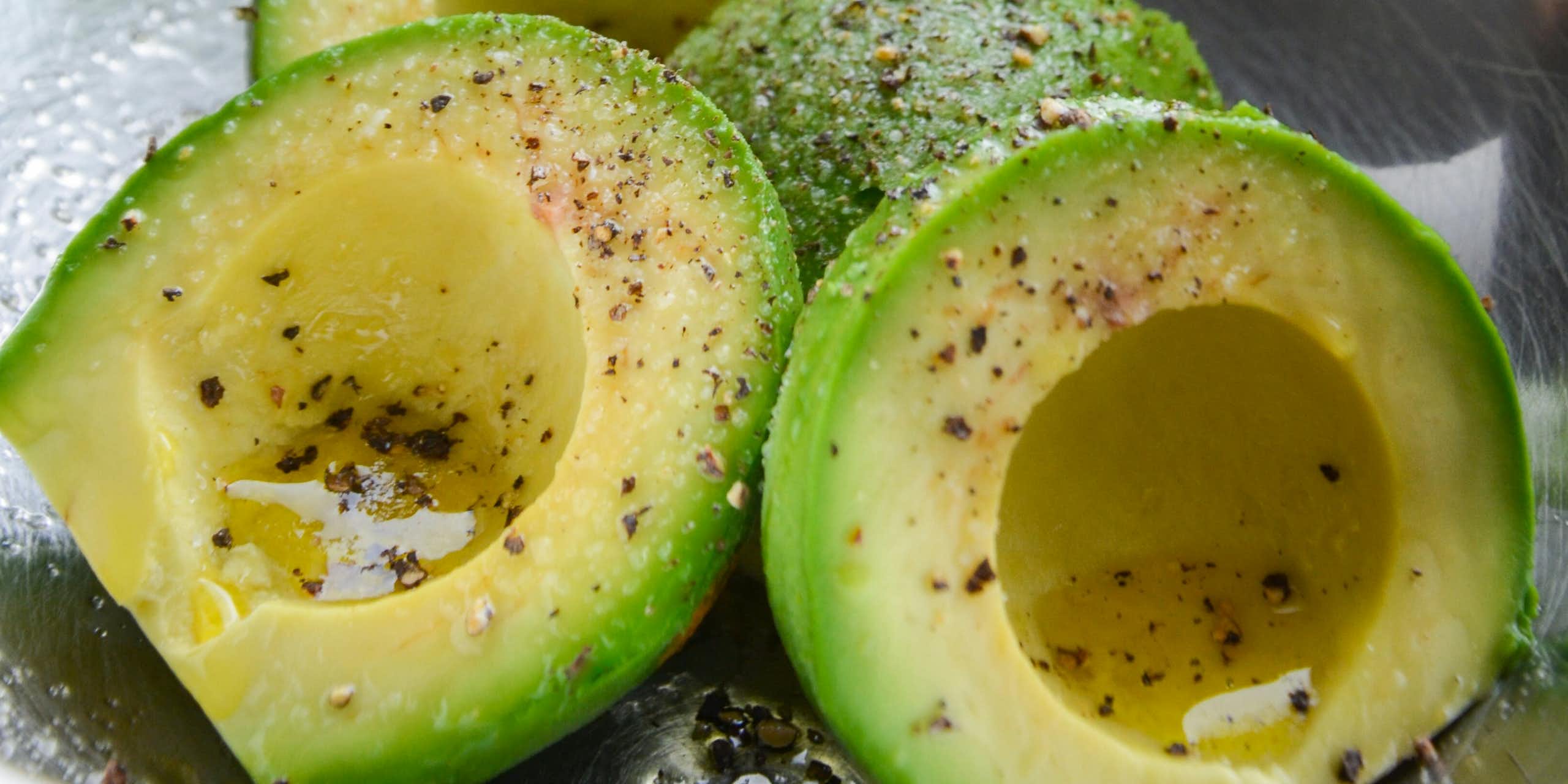 A bowl of sliced avocado drizzled with oil, salt and pepper.