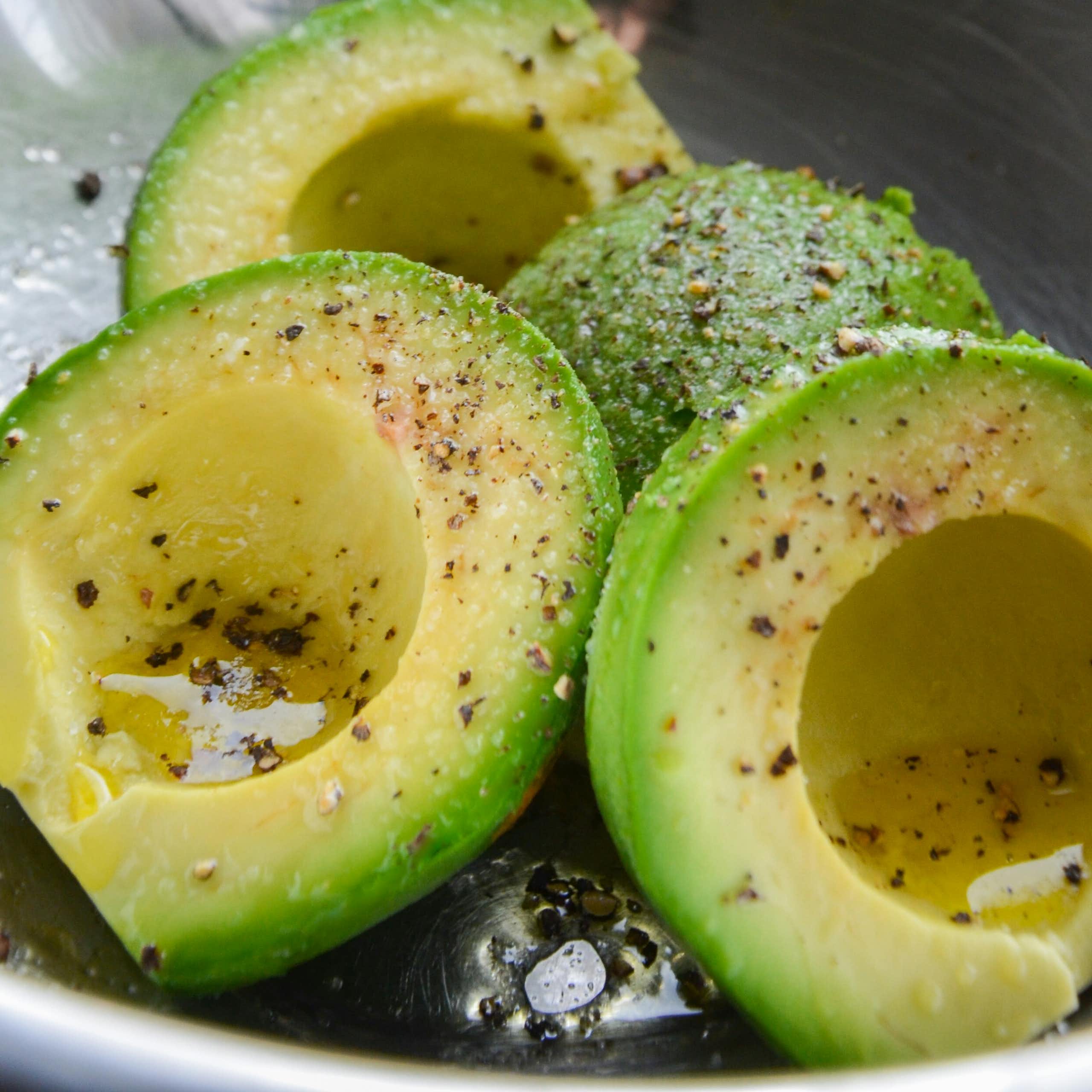 A bowl of sliced avocado drizzled with oil, salt and pepper.