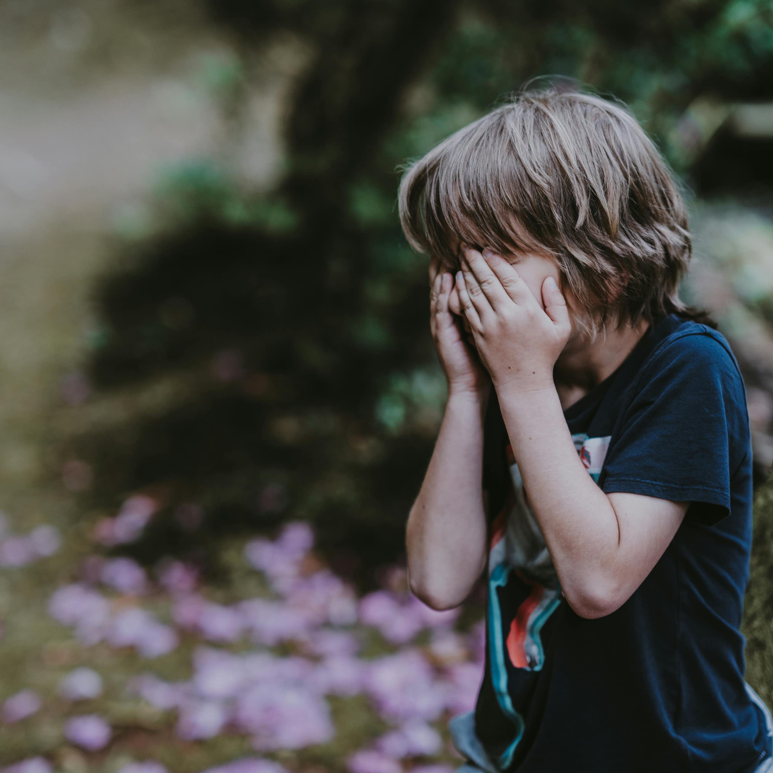 A young boy put his hands over his face. 