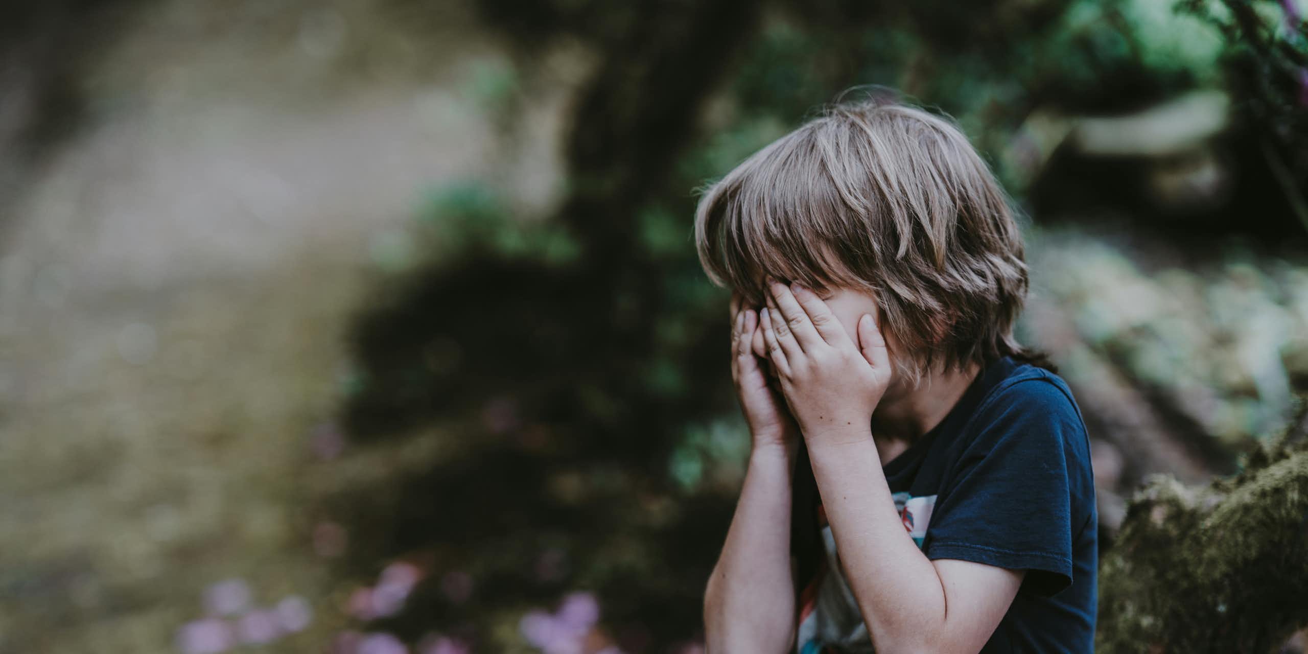 A young boy put his hands over his face. 