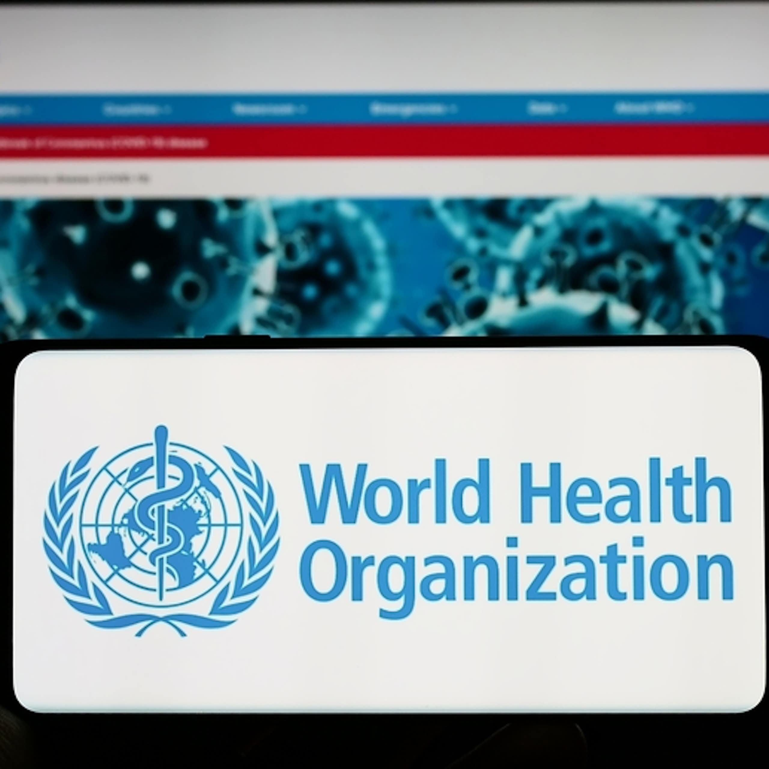 Smartphone with WHO logo held against computer screen showing WHO website