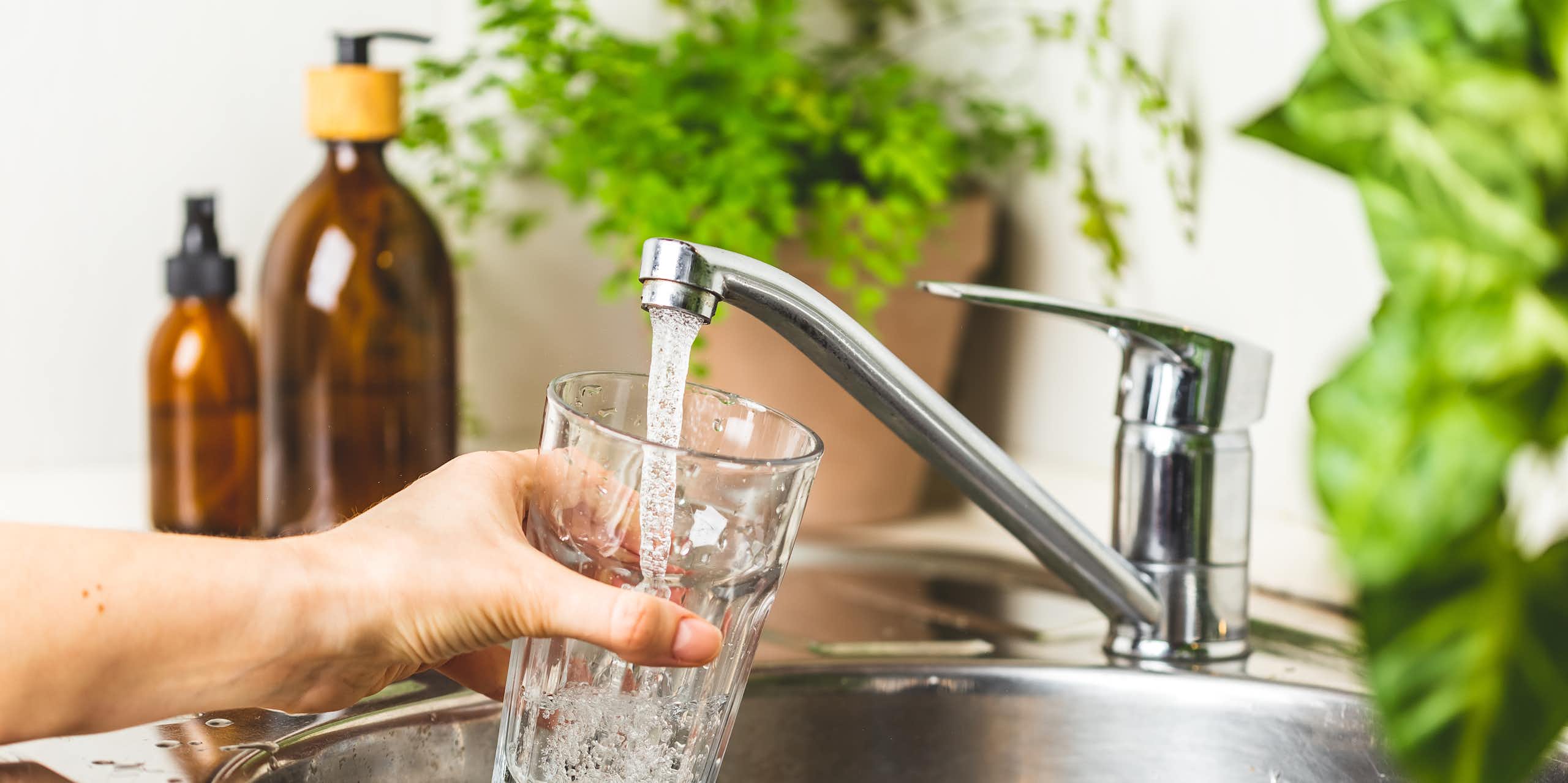 A hand filling a glass of water from the tap.