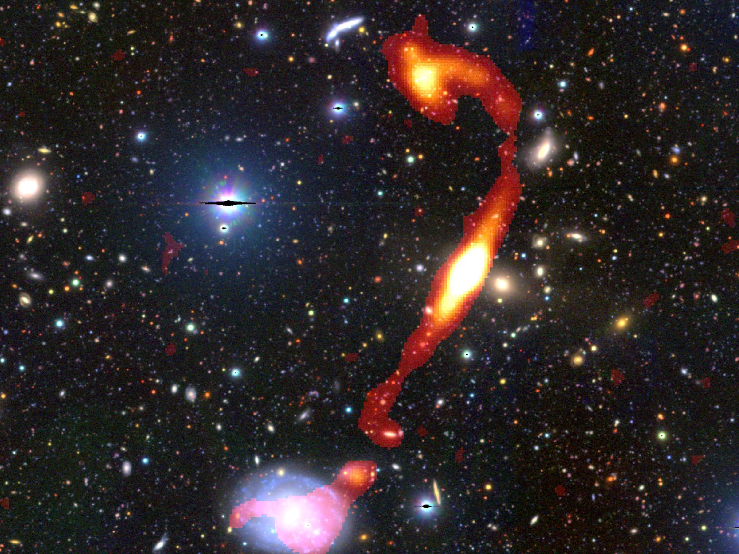 An image taken by a radio telescope of what appears to be a long tail of red and yellow emerging from a bright blur of light, surrounded by glowing red, yellow and blue lights