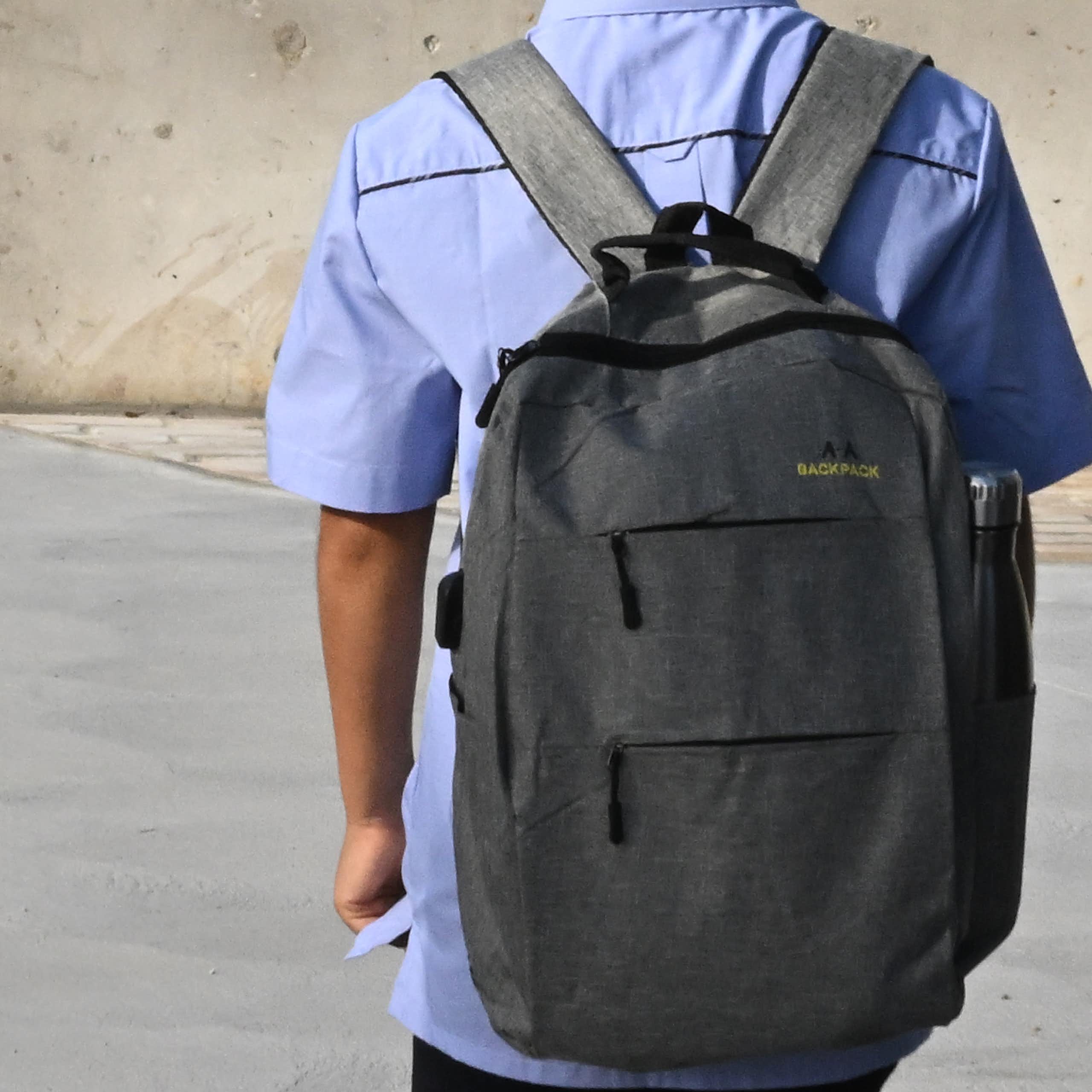 A young student in uniform with a backpack, standing on their own. 